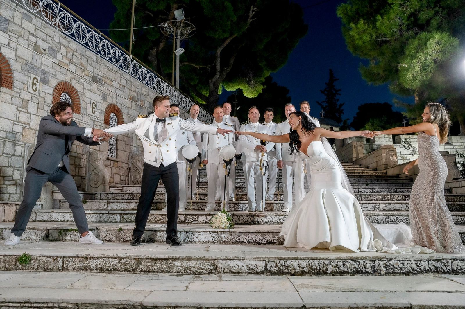 Τη νύχτα, ο γαμπρός και η νύφη τραβιούνται παιχνιδιάρικα από δύο καλεσμένους σε πέτρινα σκαλιά με ναυτικούς.