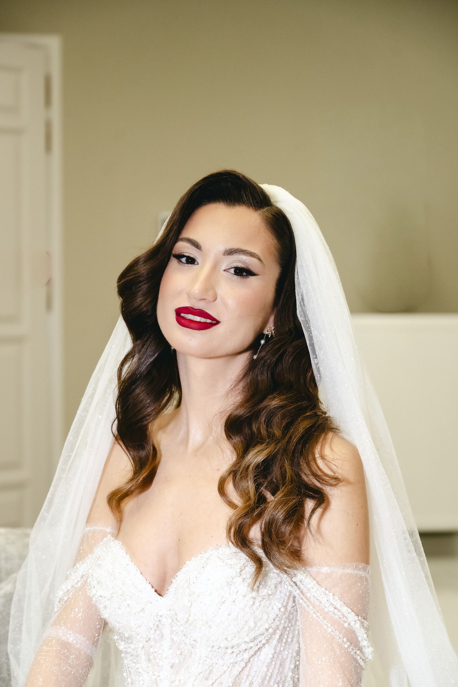 The bride with a veil, wavy hair and red lipstick in a bright room