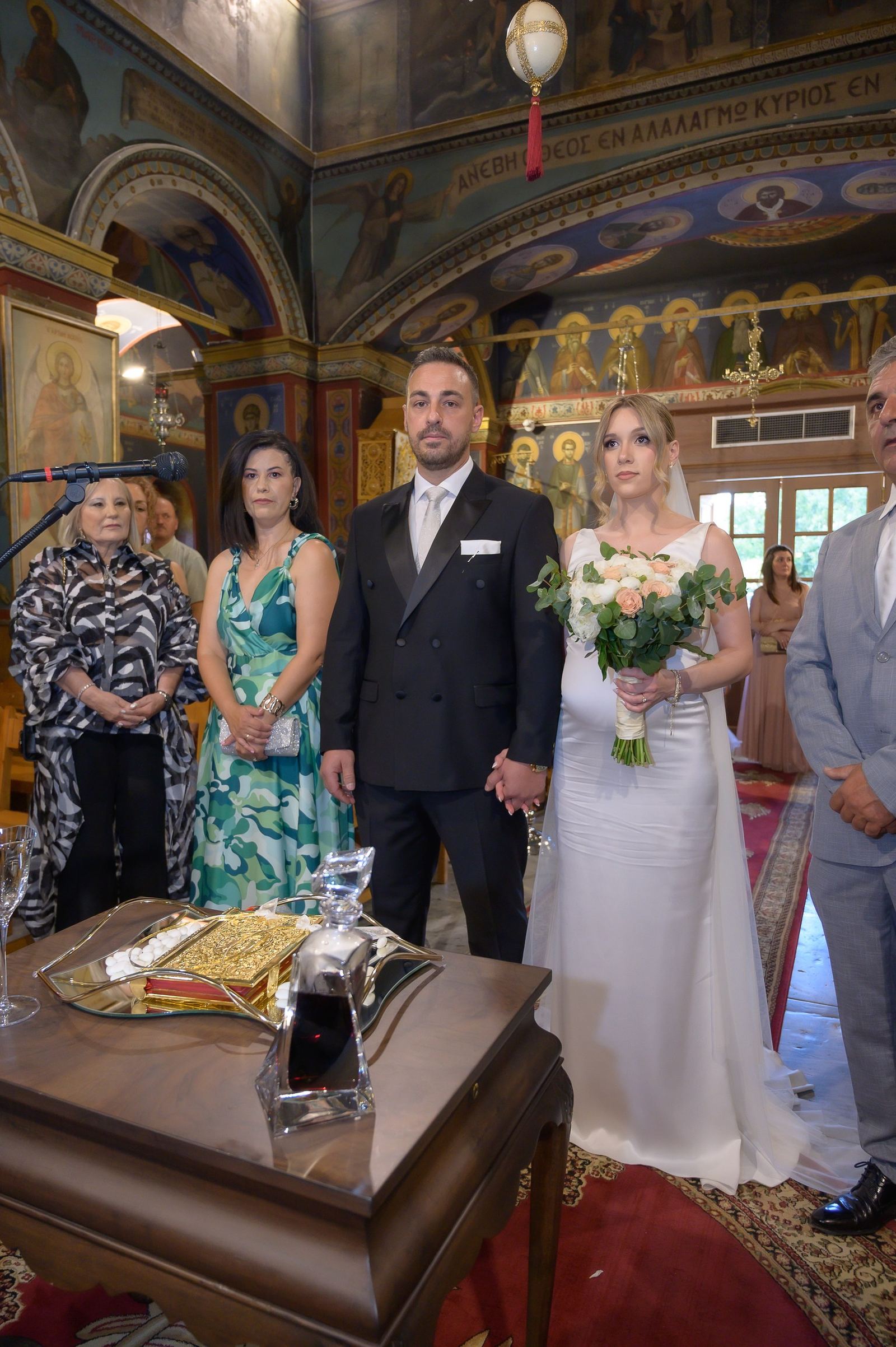 The bride and groom hold hands at the ceremony table inside a church covered in painted icons.