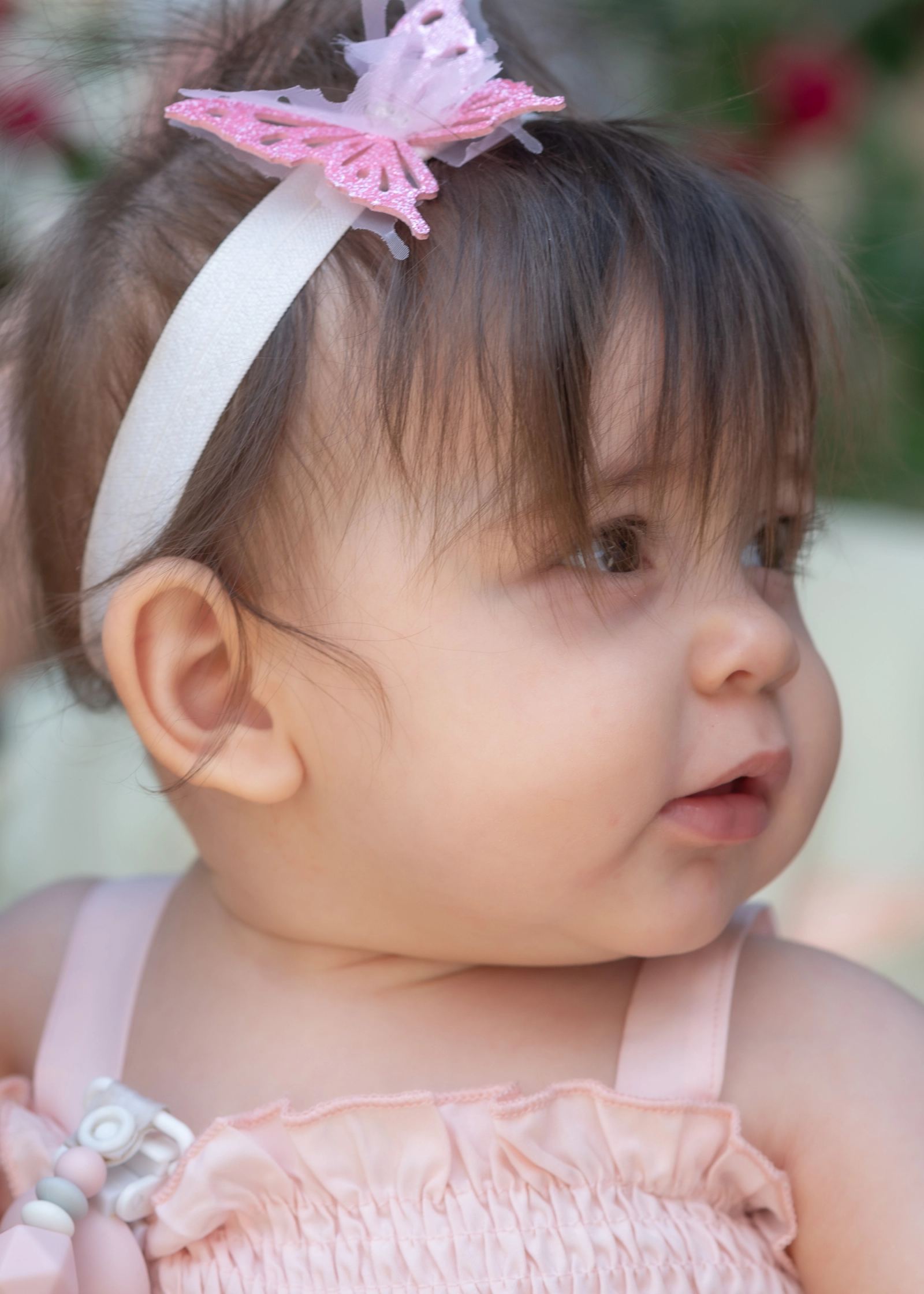 Close-up of the baby in a pink dress and a headband with a pink butterfly, looking to the side.