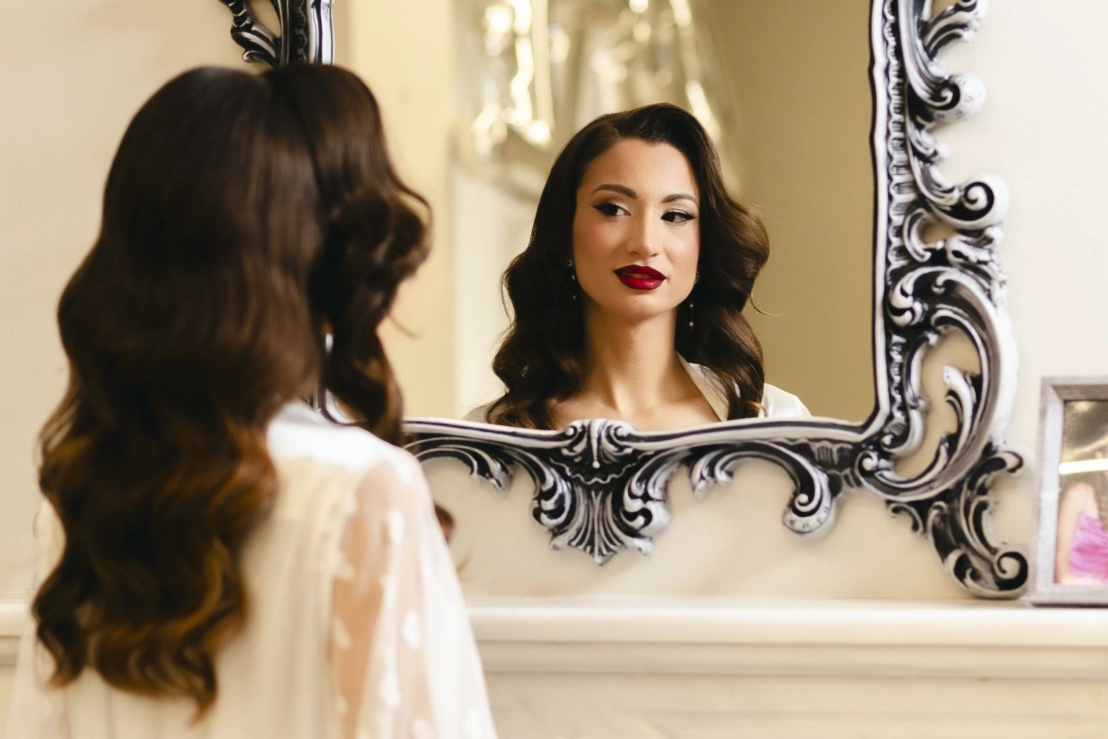 The bride with wavy hair and red lipstick reflected in an ornate silver mirror
