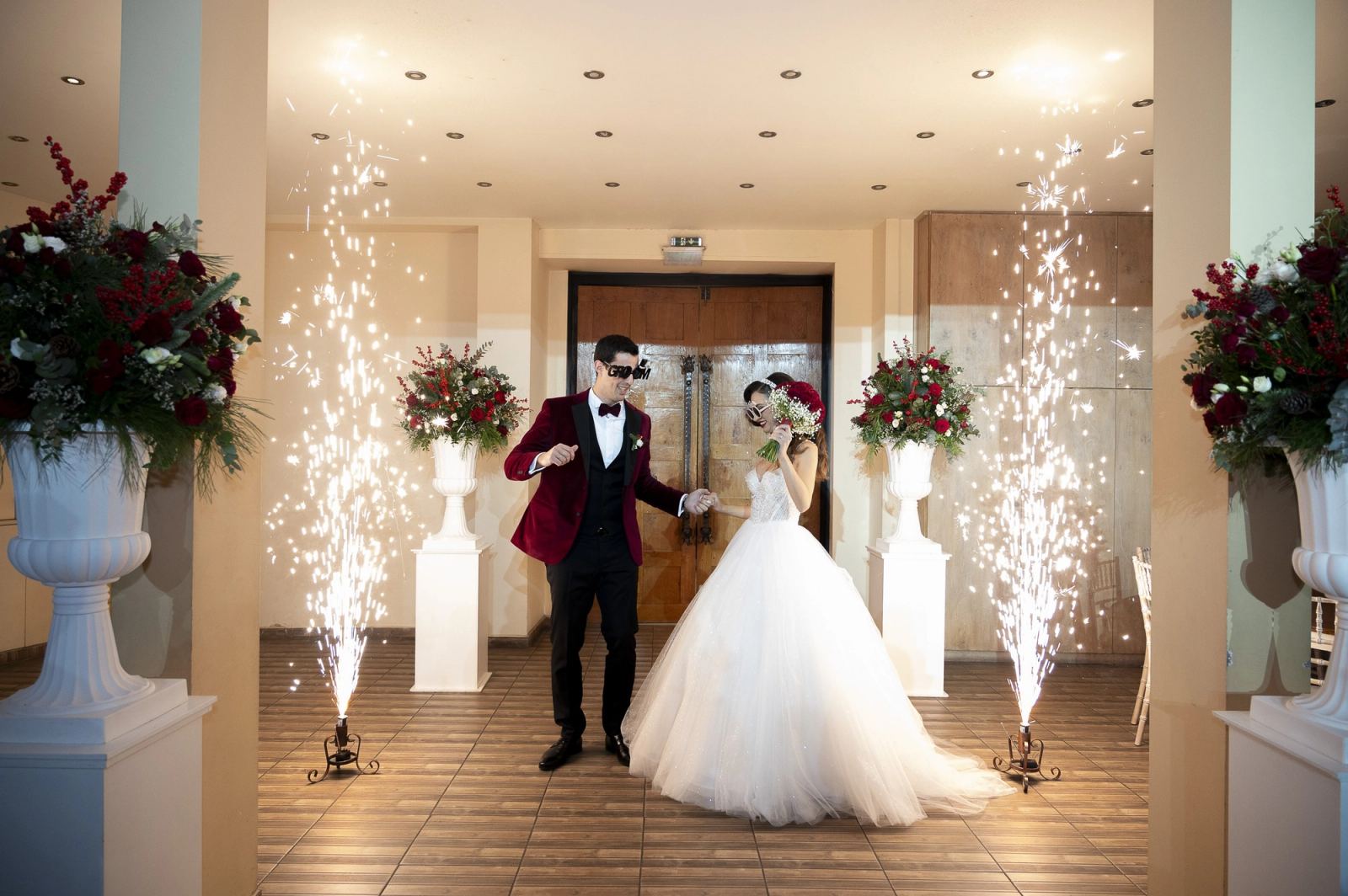 The bride and groom, in novelty glasses, walk in between two fountains of sparks.