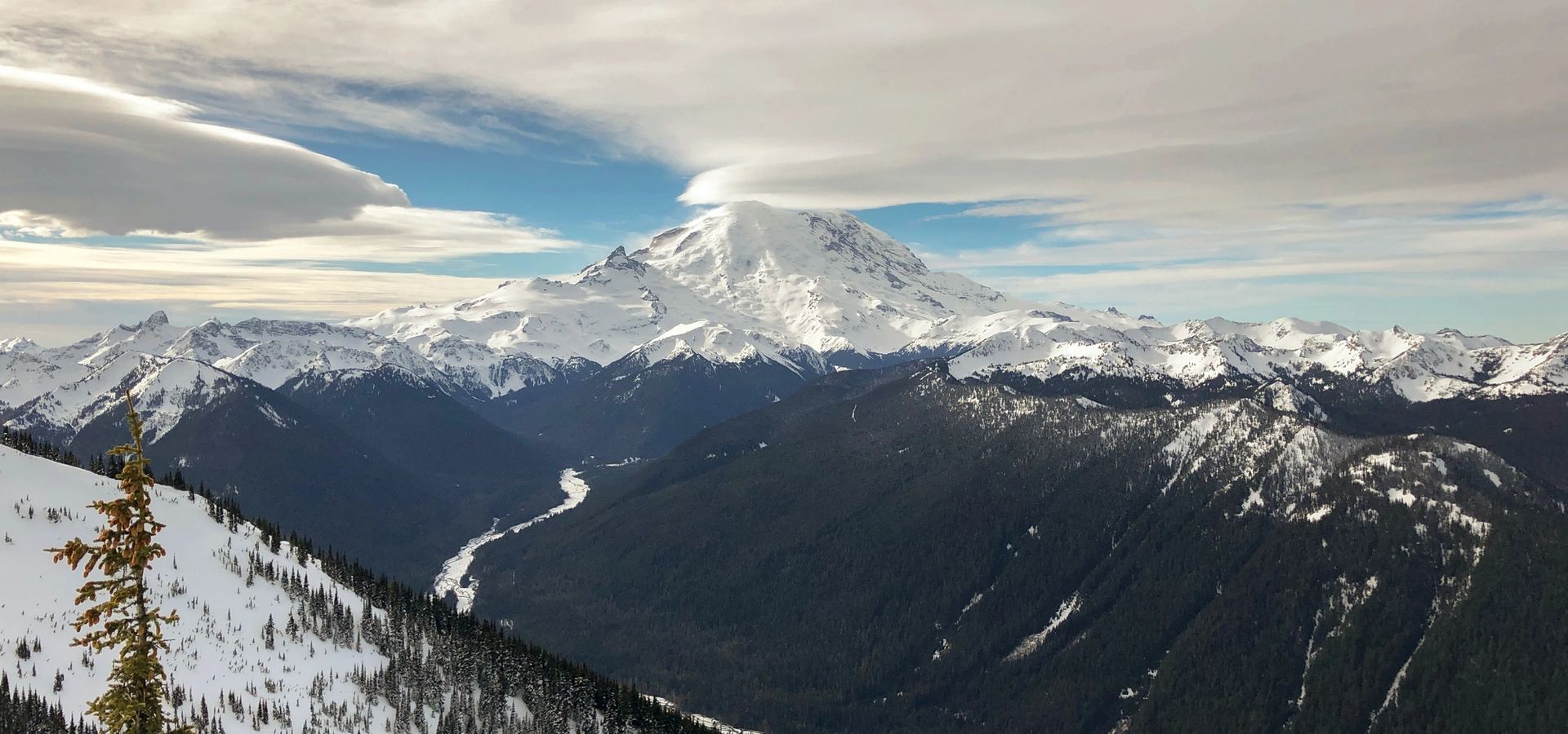 Mount Rainier under dramatic lenticular clouds with a snow-streaked valley below — long horizons, high aspirations.