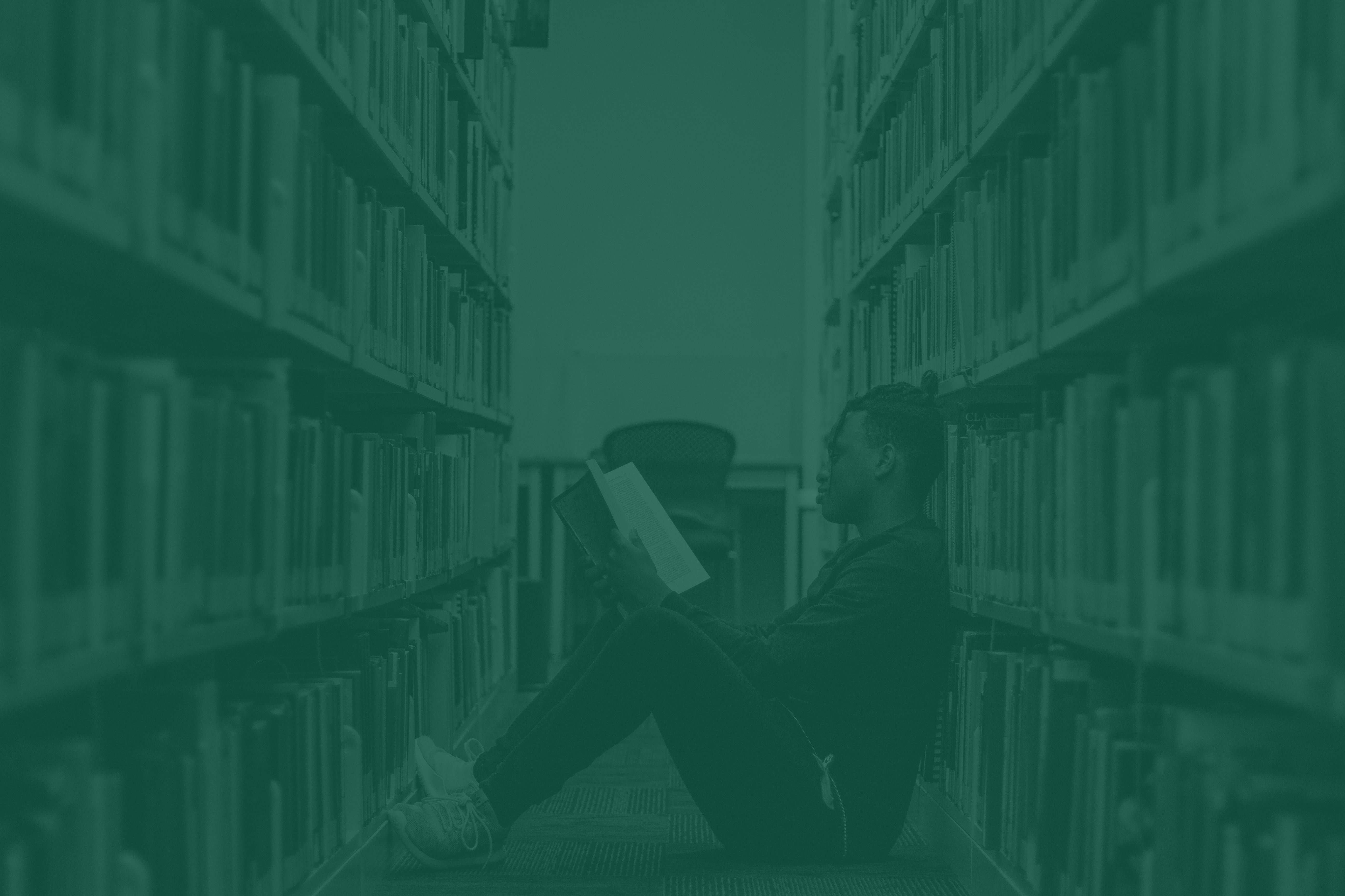 A person sitting on the floor reading in a library aisle.