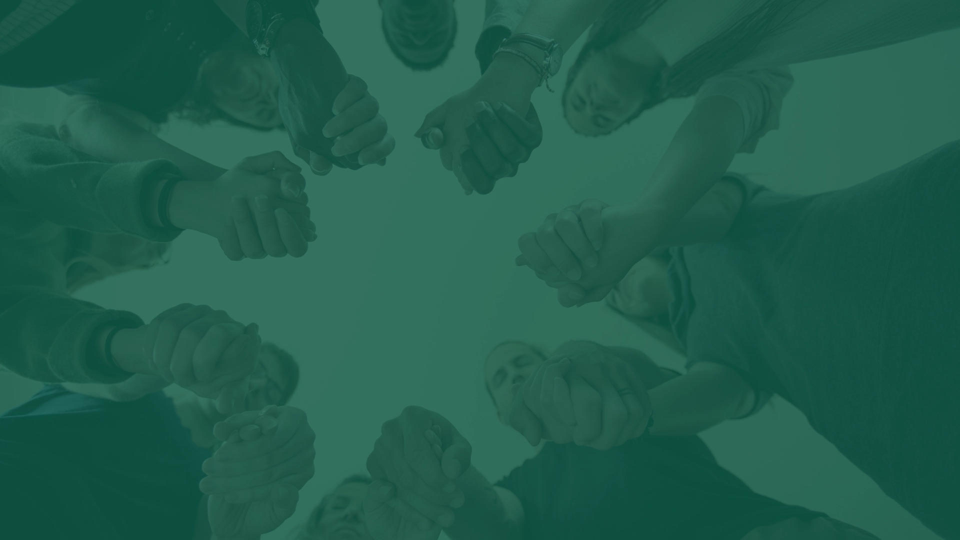 A circle of people standing together with hands clasped in prayer.
