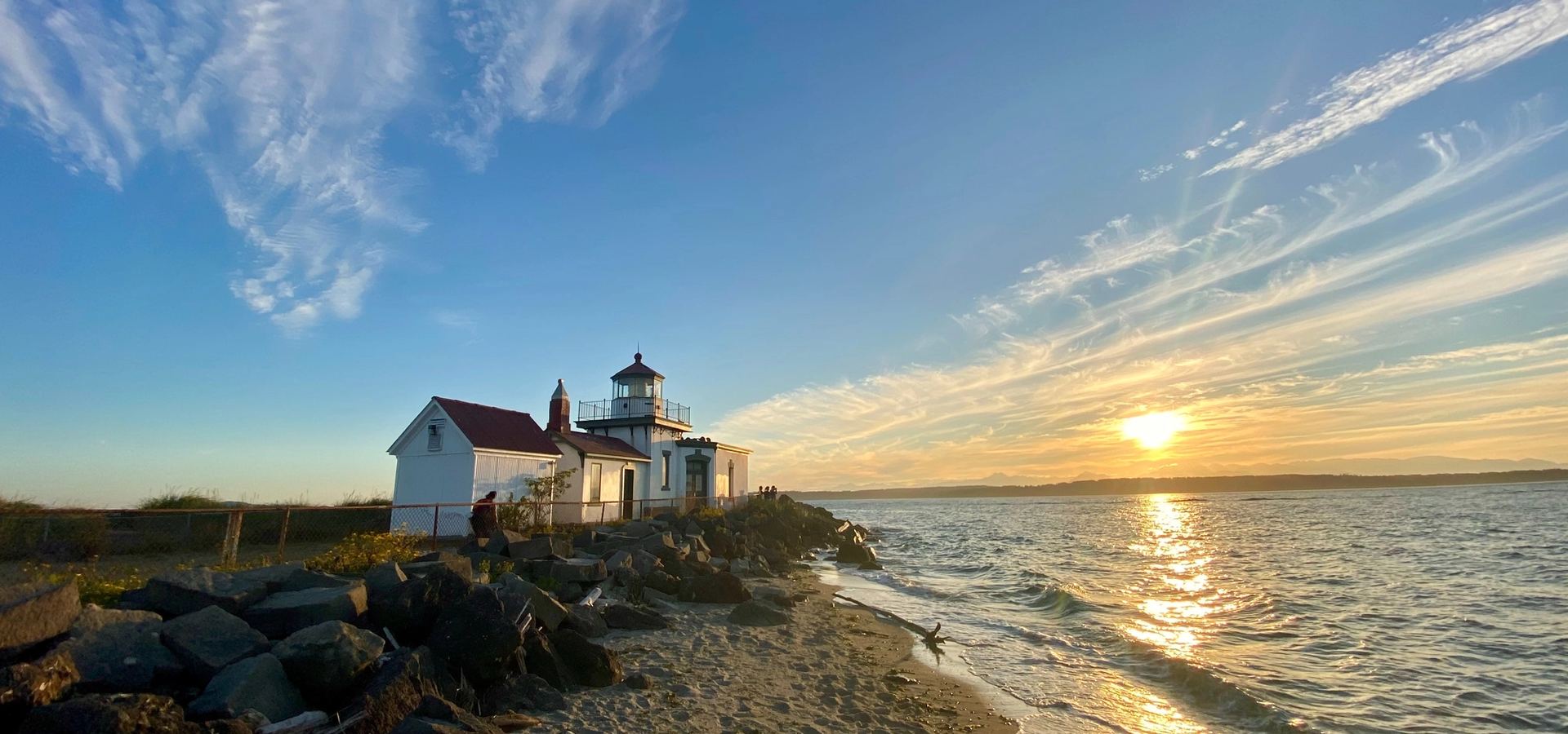 A lighthouse at sunset on a Pacific Northwest beach with calm water — anchored, dependable, watchful.