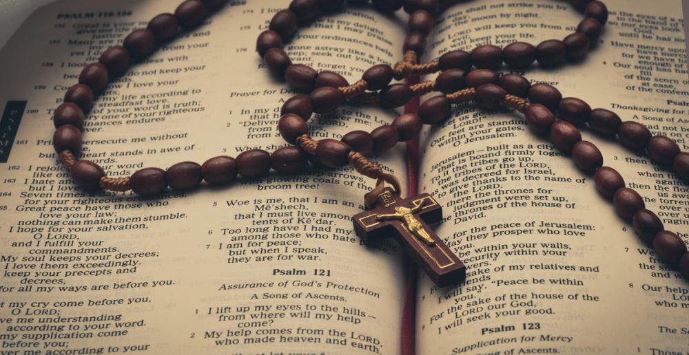 An open Bible with a wooden rosary resting on its pages, symbolizing resources for Catholic faith and study.