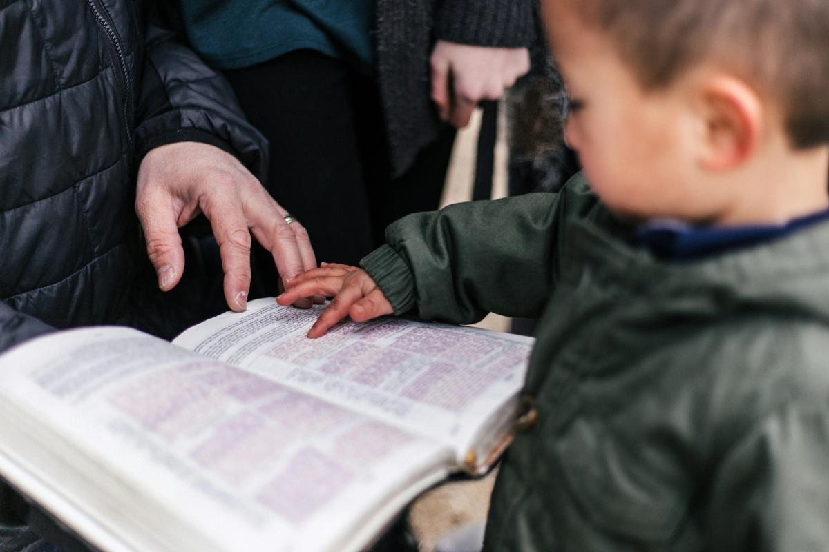 A young child and grandparent both looking at a bible together