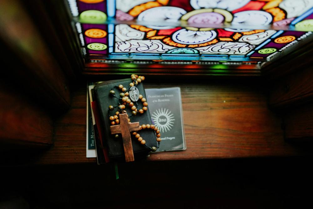 A Catholic Bible by a Church Stained Glass Window with a Rosary on top of it