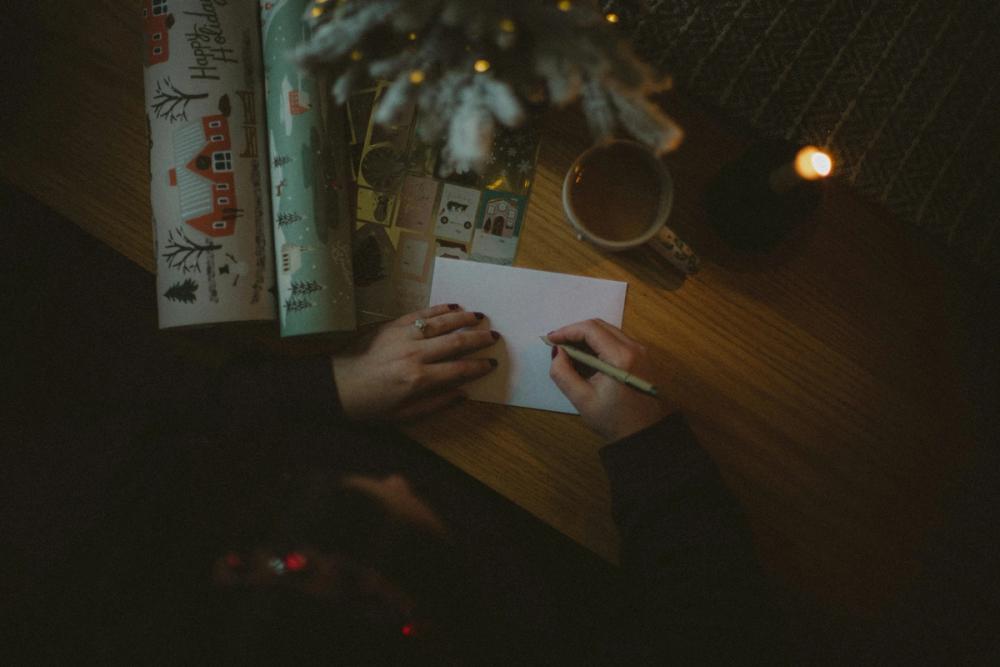 Writing in a Christian Christmas card, surrounded by wrapping paper and decorations, it is festive and cosy