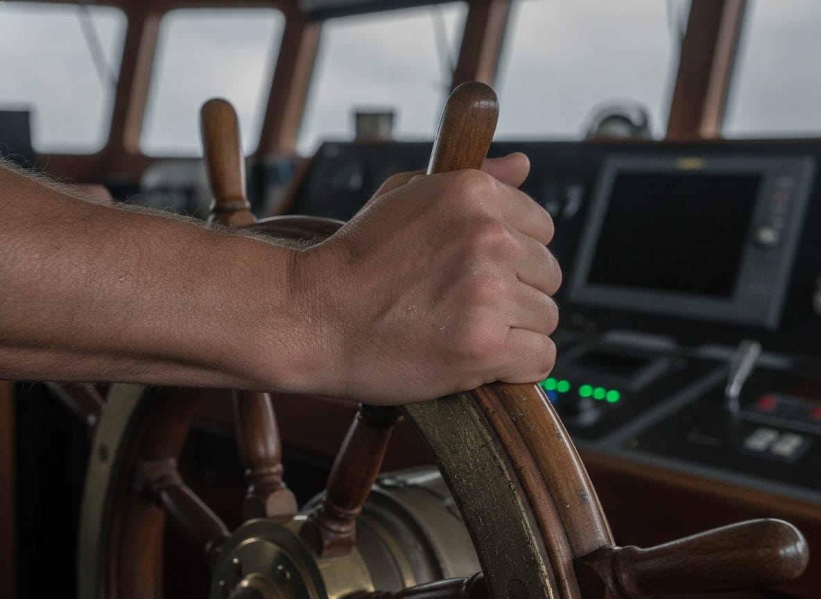 A close-up, photorealistic image of a seafarer's hands gripping a worn steering wheel, conveying the pressure of the job.