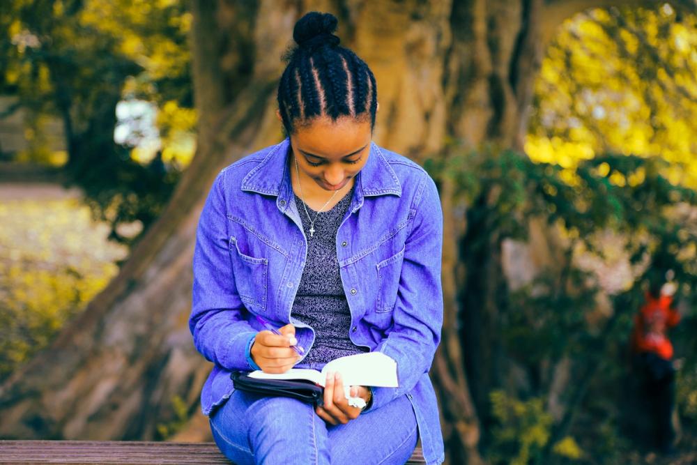 A woman in a bright outdoor setting happily reading her Bible