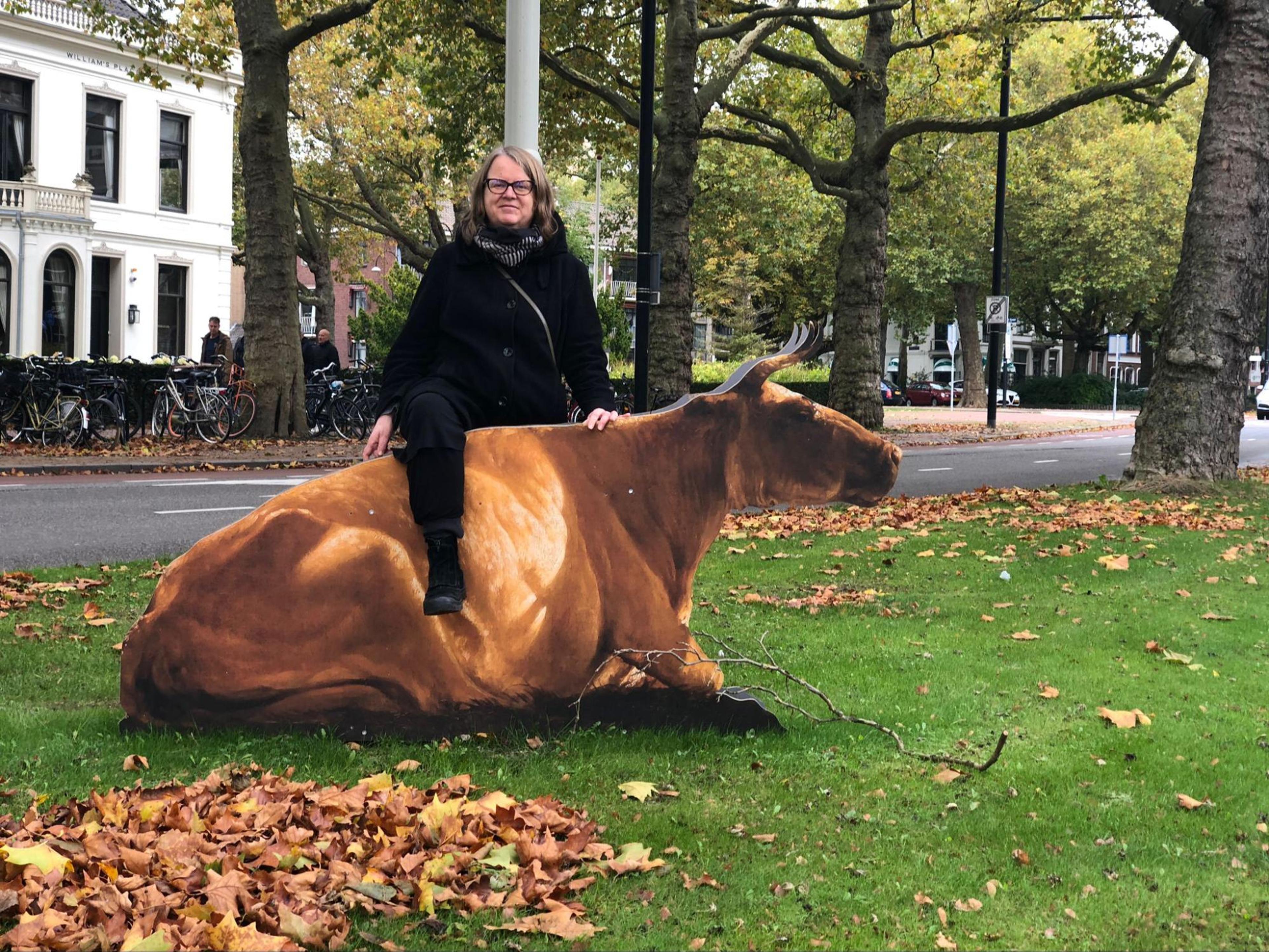 a woman posing next to cow installation somewhere in the city