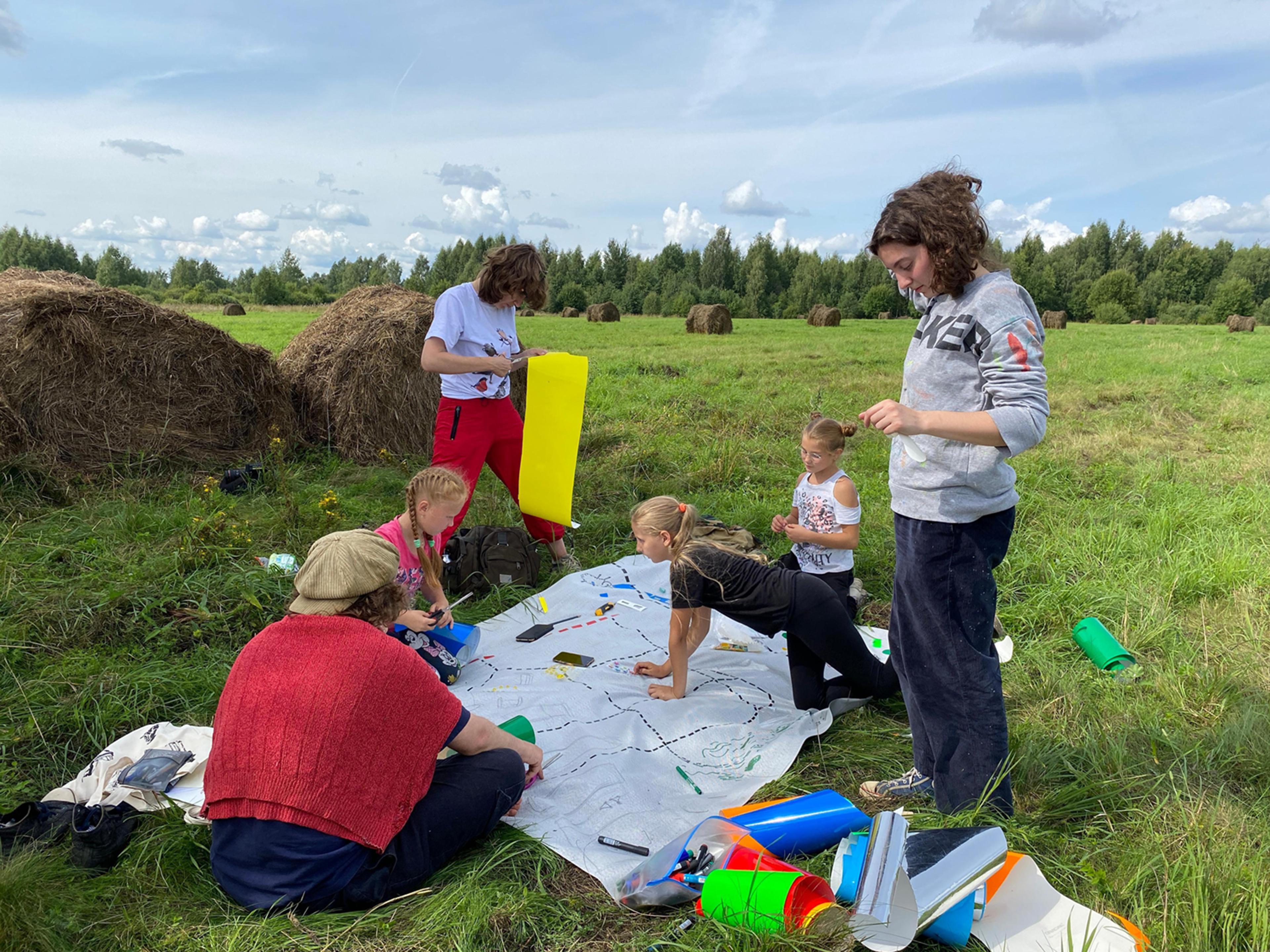 group of kids and adults working on crafts in the middle of green fields. 
