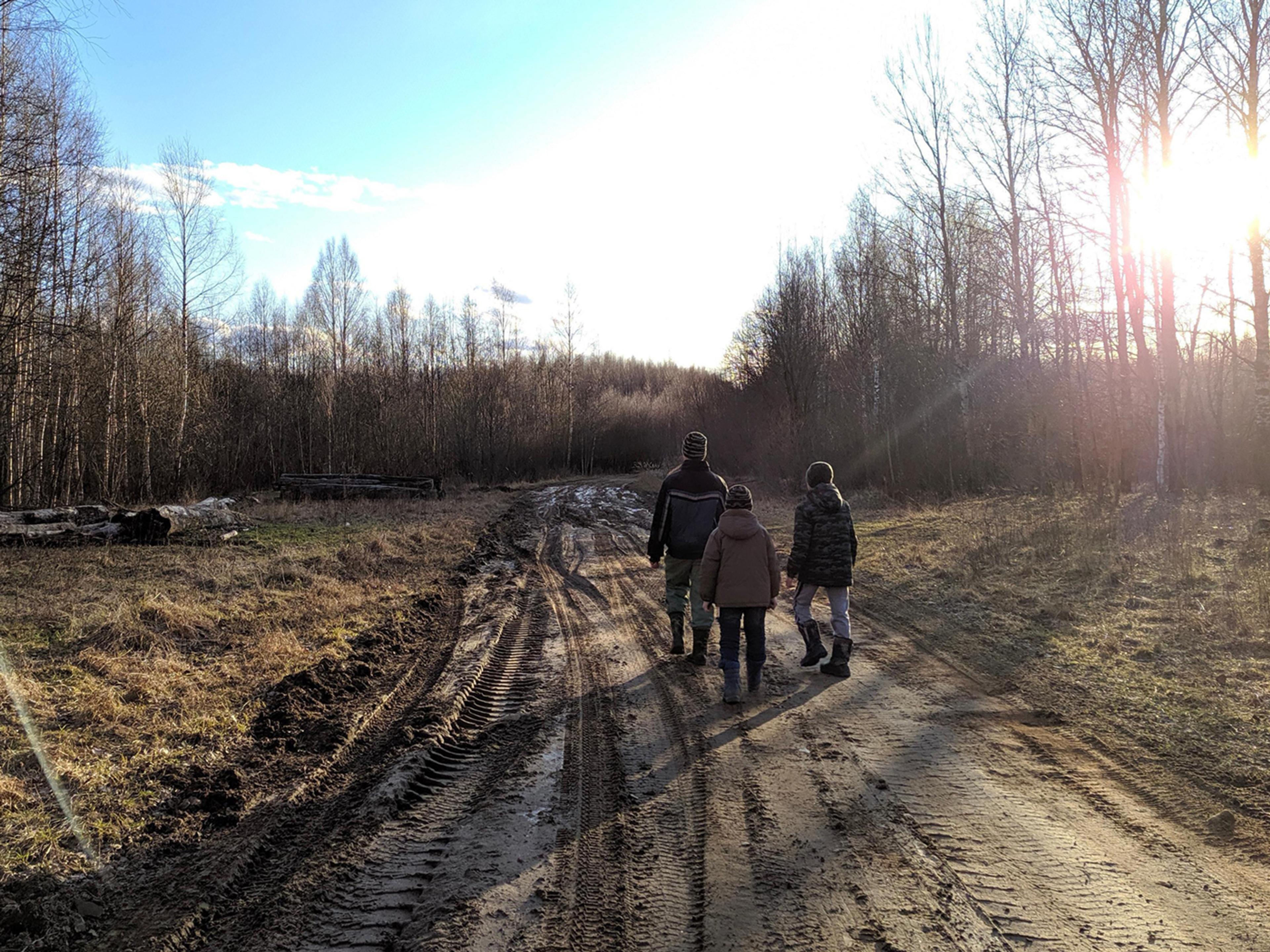 Snapshot of 3 youngsters walking on a muddy dirt road, It is sunny early spring day