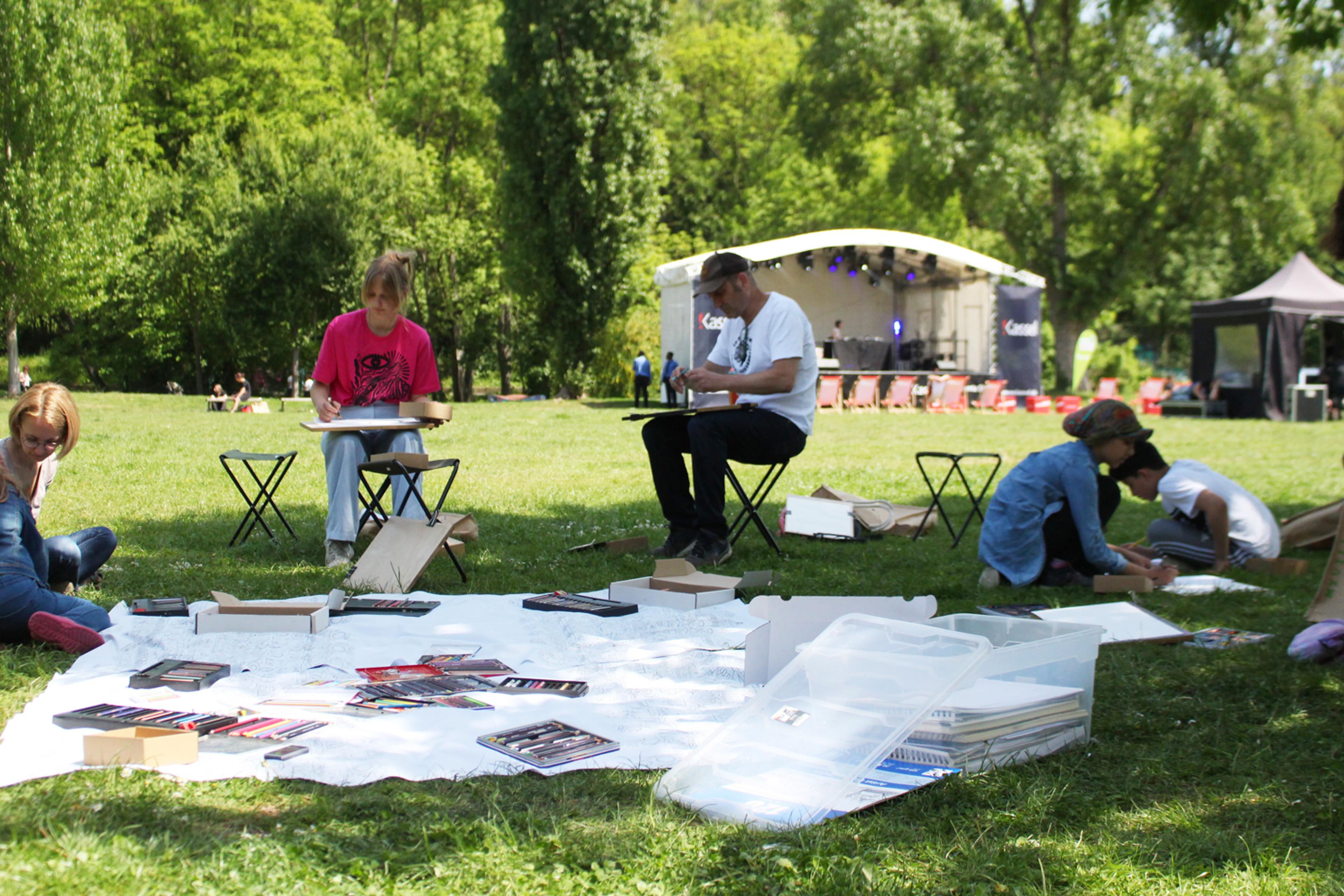A picknick? No there are drawing materials and 5 people at folded chairs making drawings in a park.