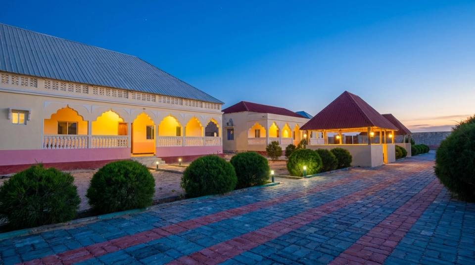 Iftin Hotel at dusk: arched verandas lit up, a garden pavilion and a paved path lined with shrubs.