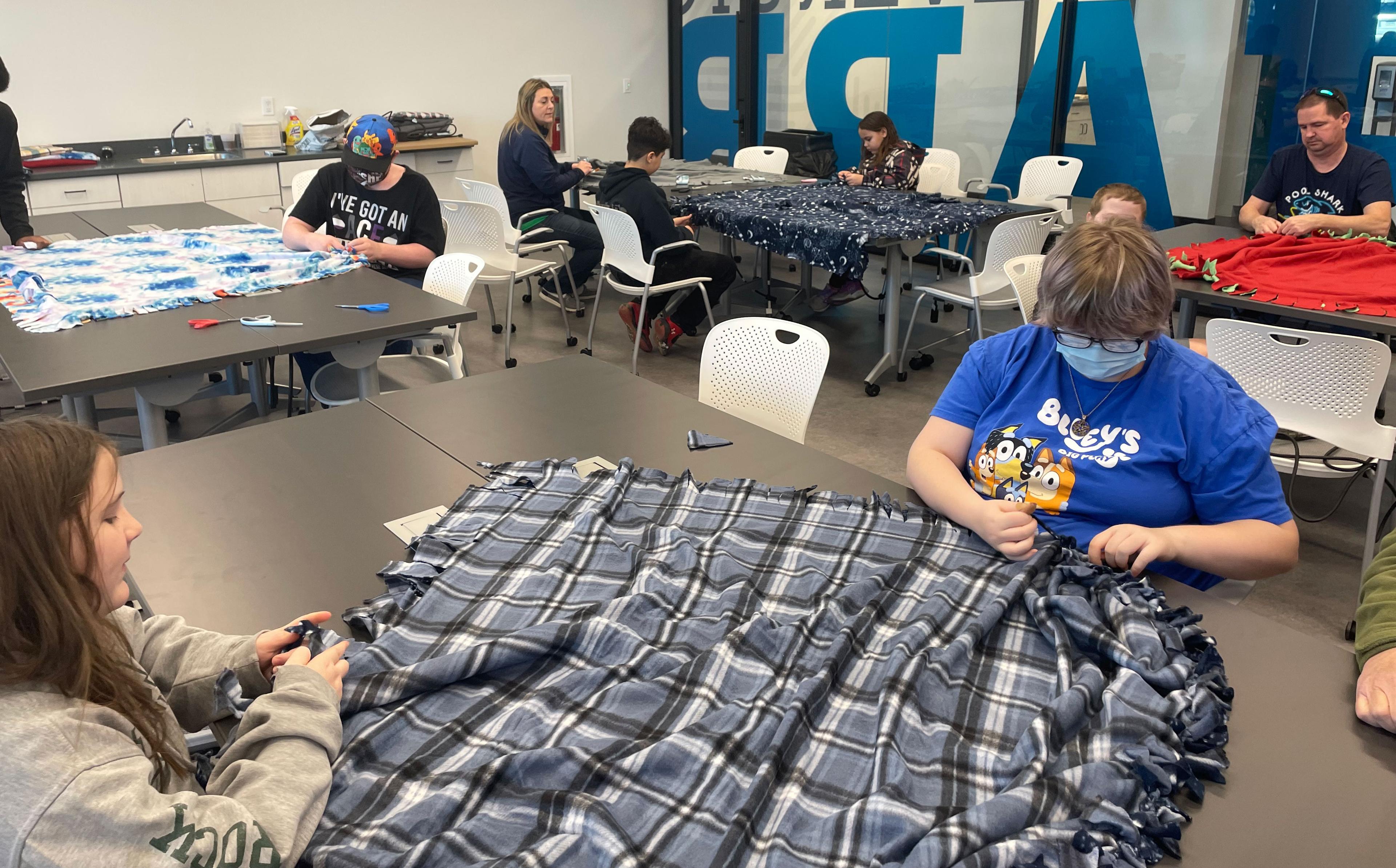 Two students work on a no-sew blanket for a homeless shelter