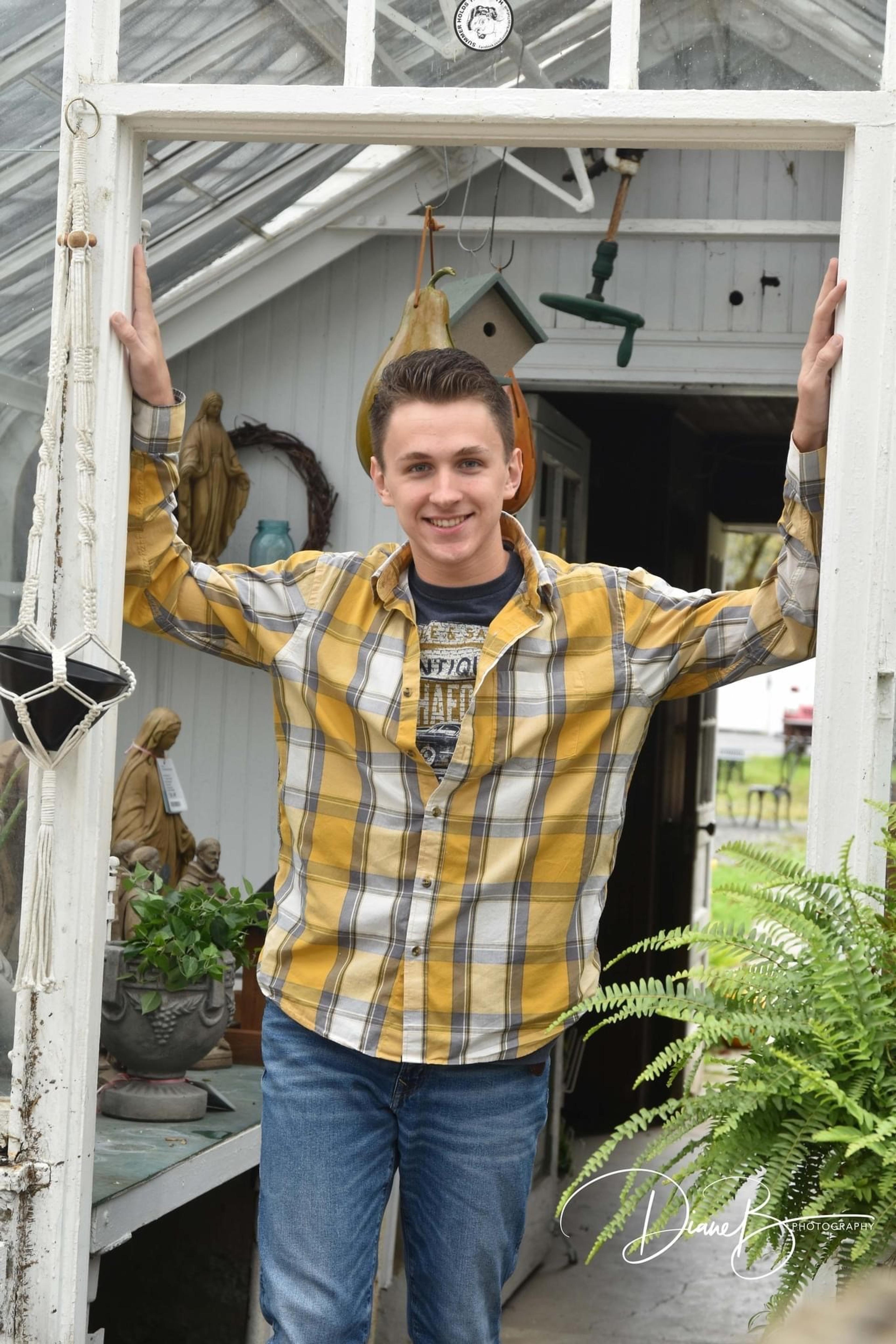 High school senior poses in a rustic building. He's wearing a yellow and white plaid shirt and jeans. 