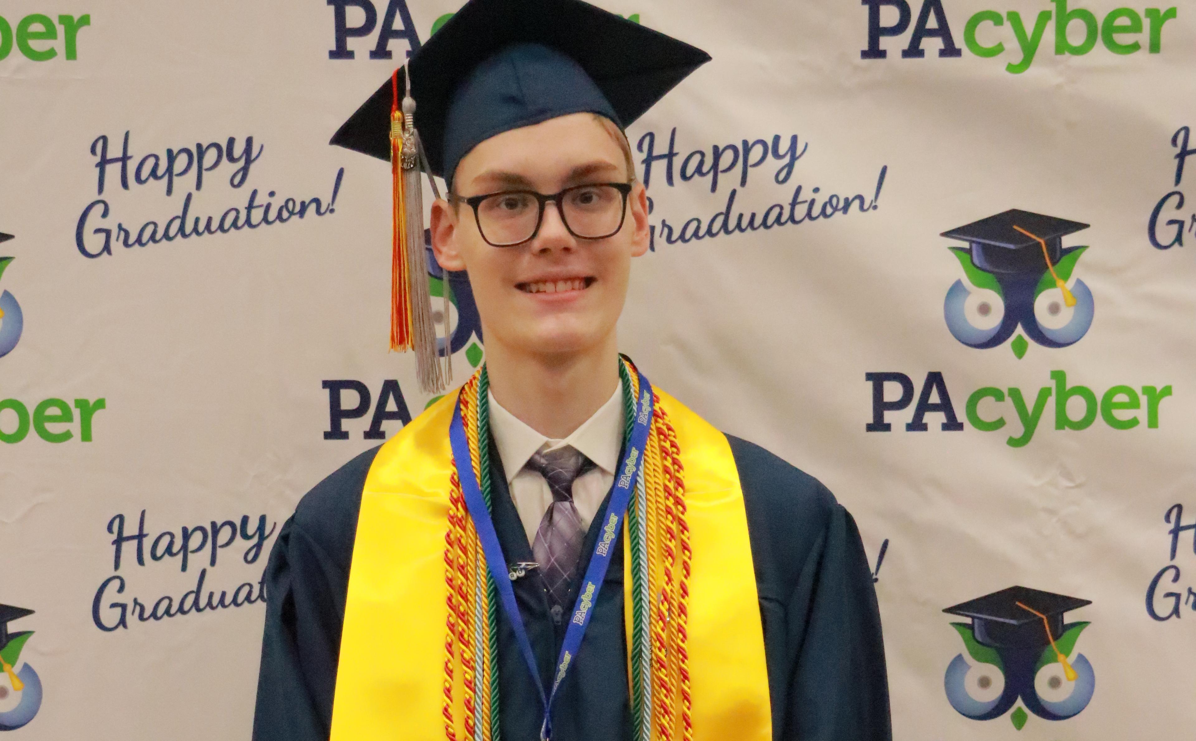 PA Cyber graduate wears cap and gown and several colorful cords.