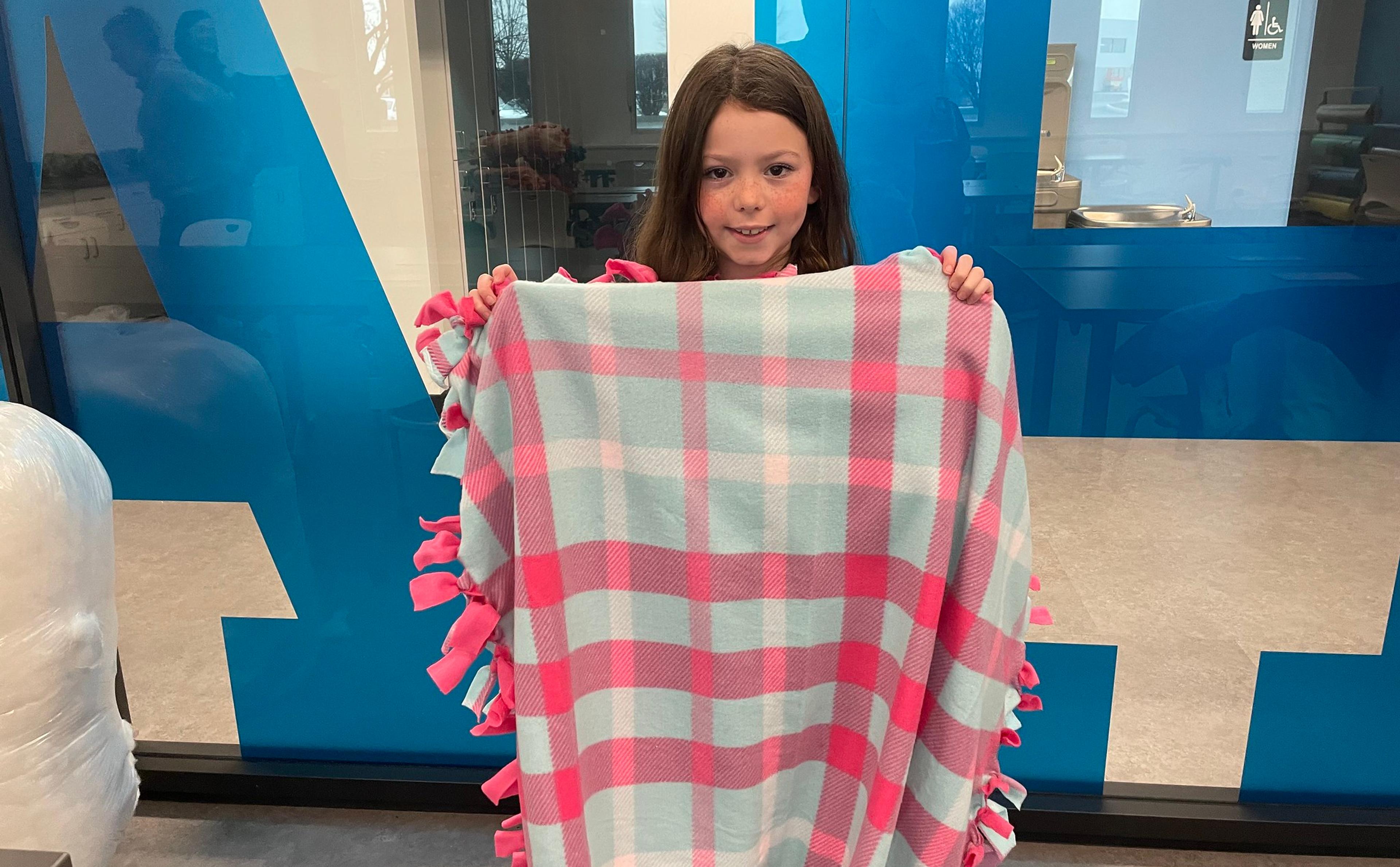 Young girl holds a pink and blue plaid blanket.