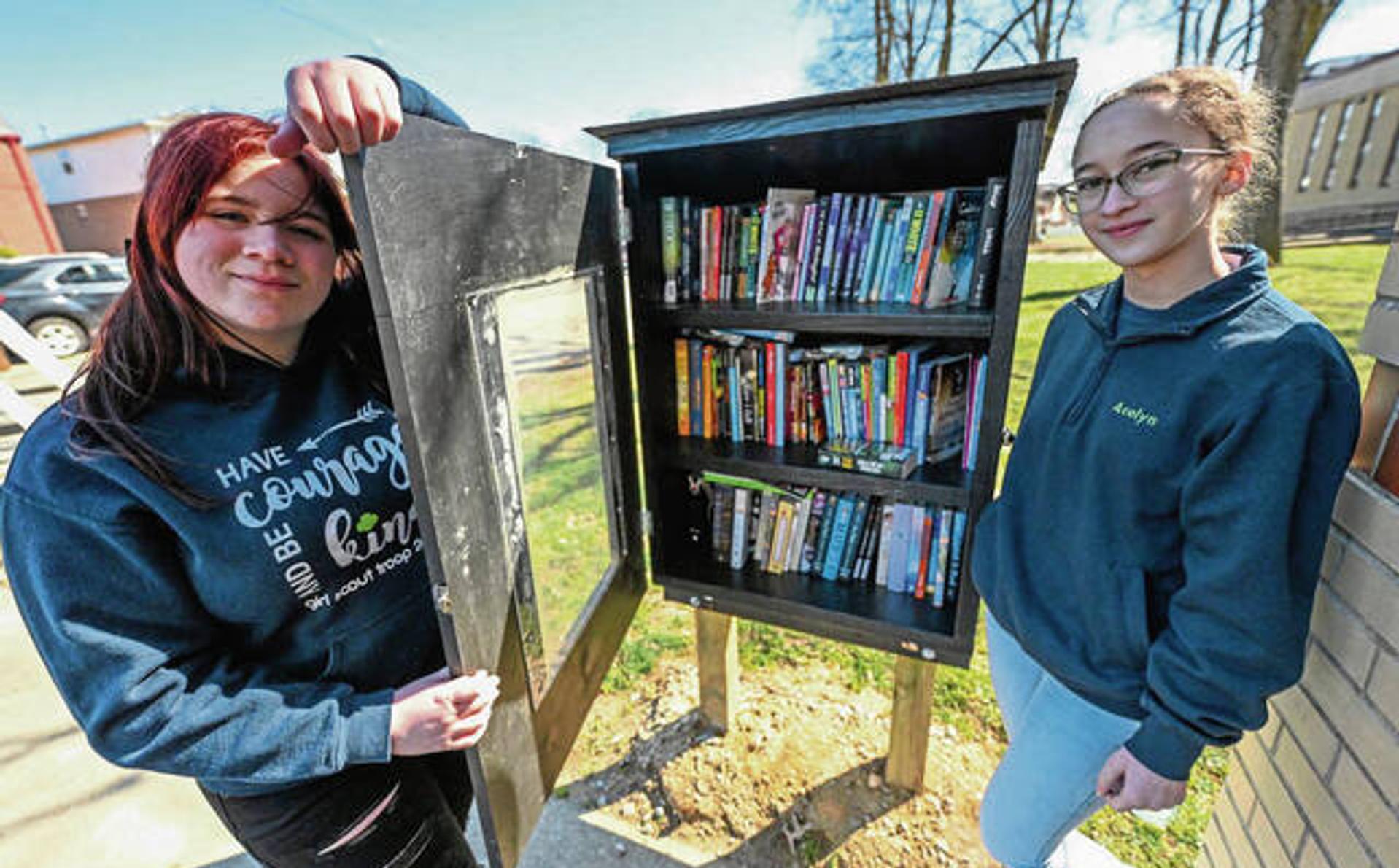 Two teenage girls standing next to a little free library box.