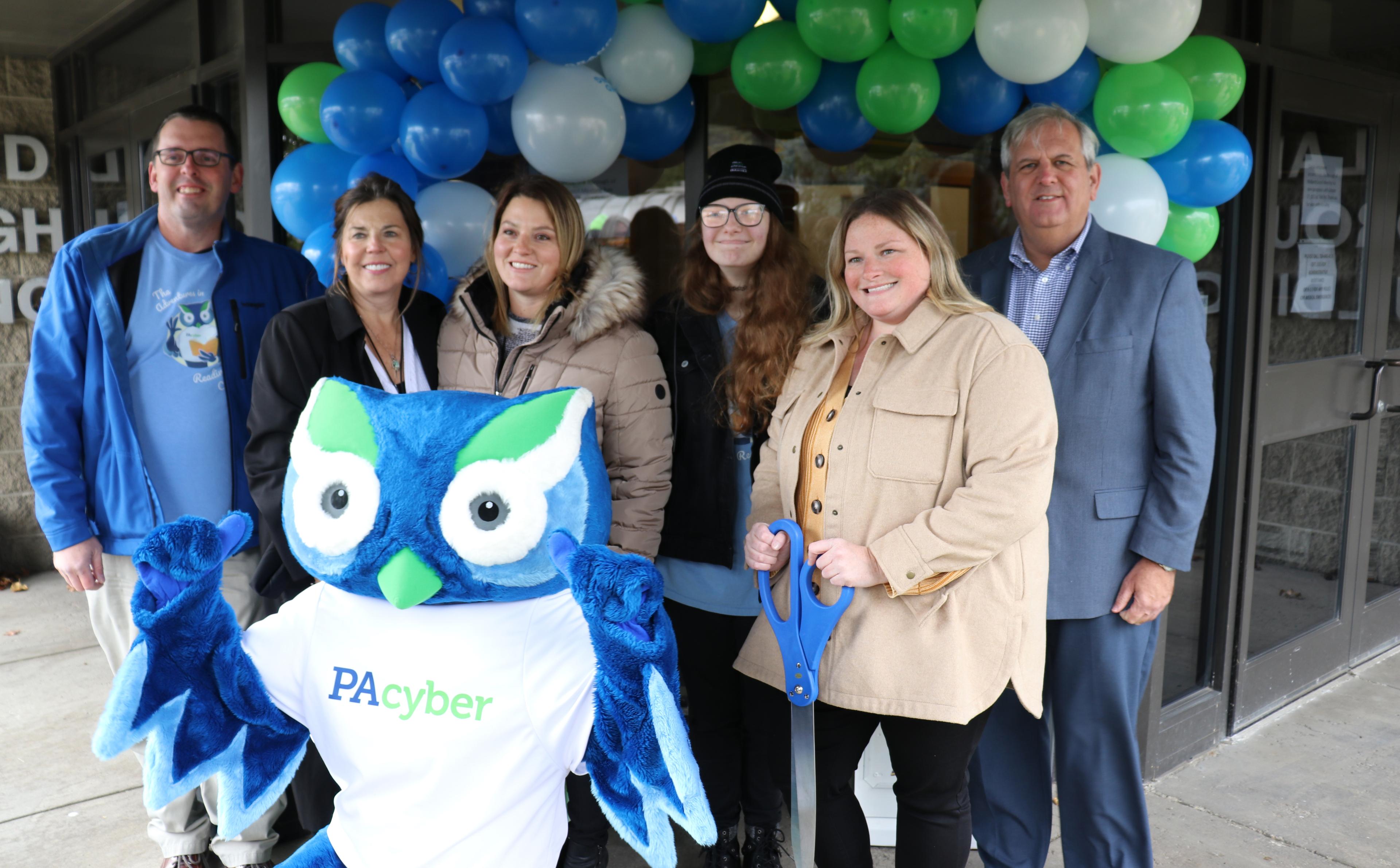 Six PA Cyber employees pose with mascot Archie the Owl in front of balloons.