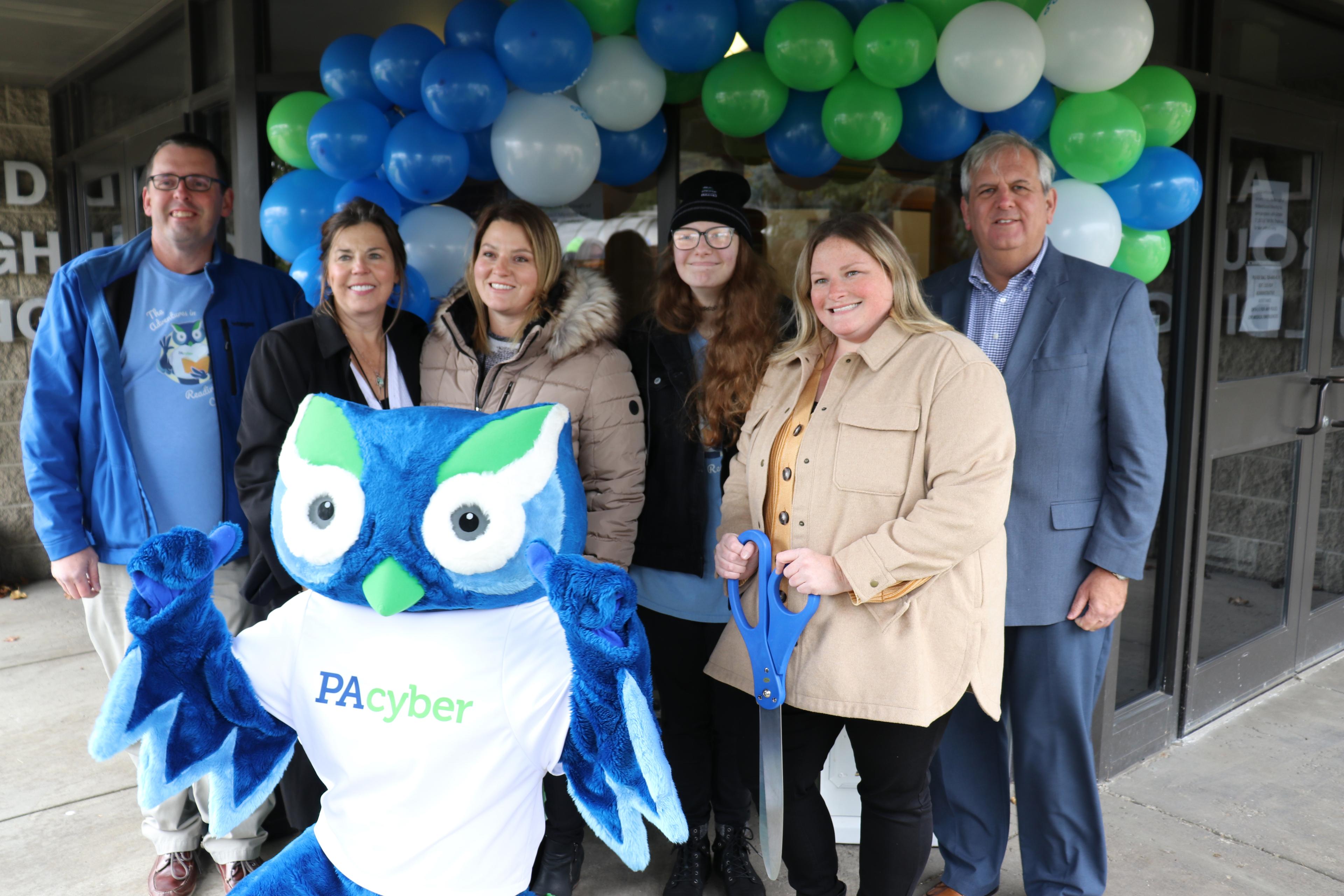 Six PA Cyber employees pose with mascot Archie the Owl in front of a balloon arch.