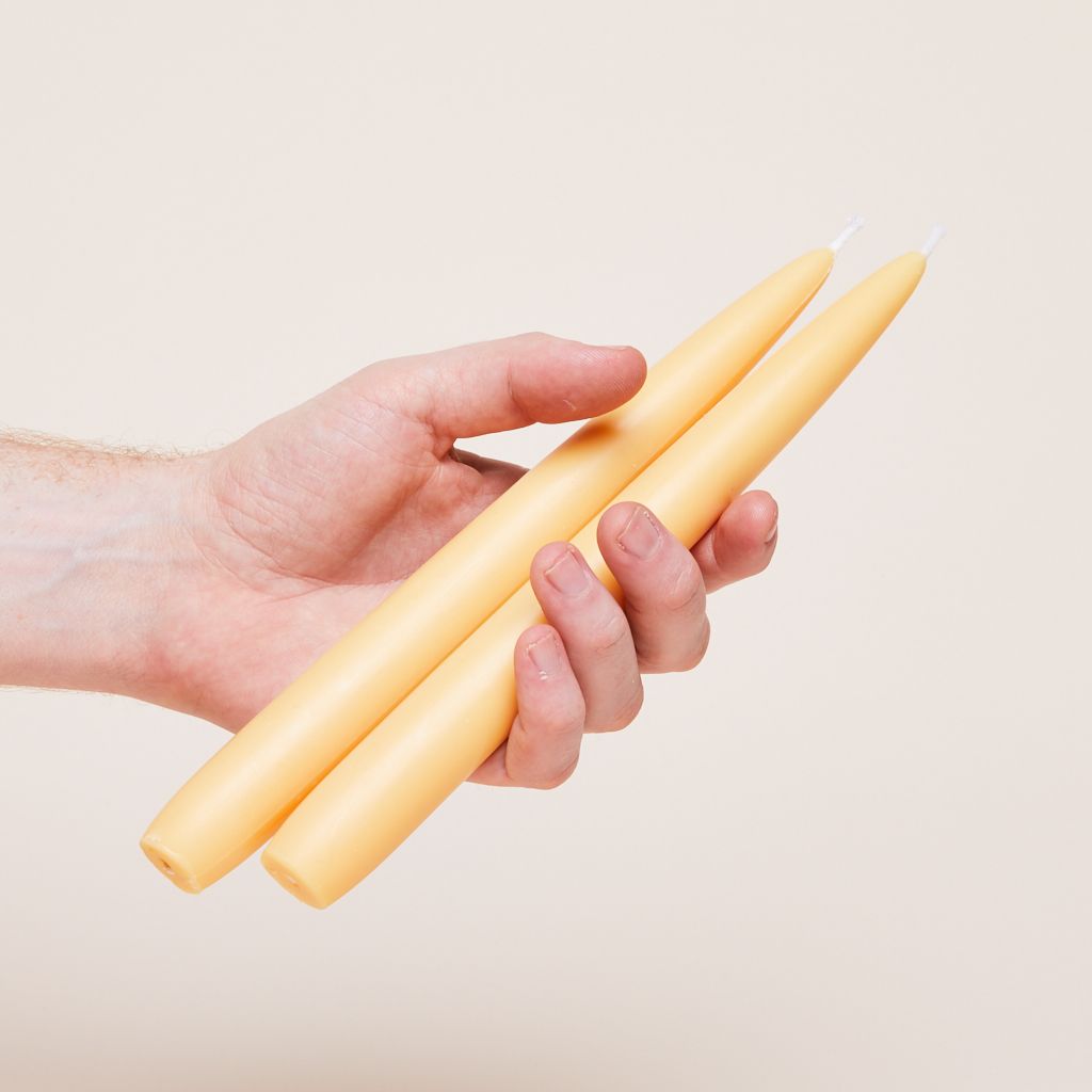 Two long, thin unlit candles are held in a hand