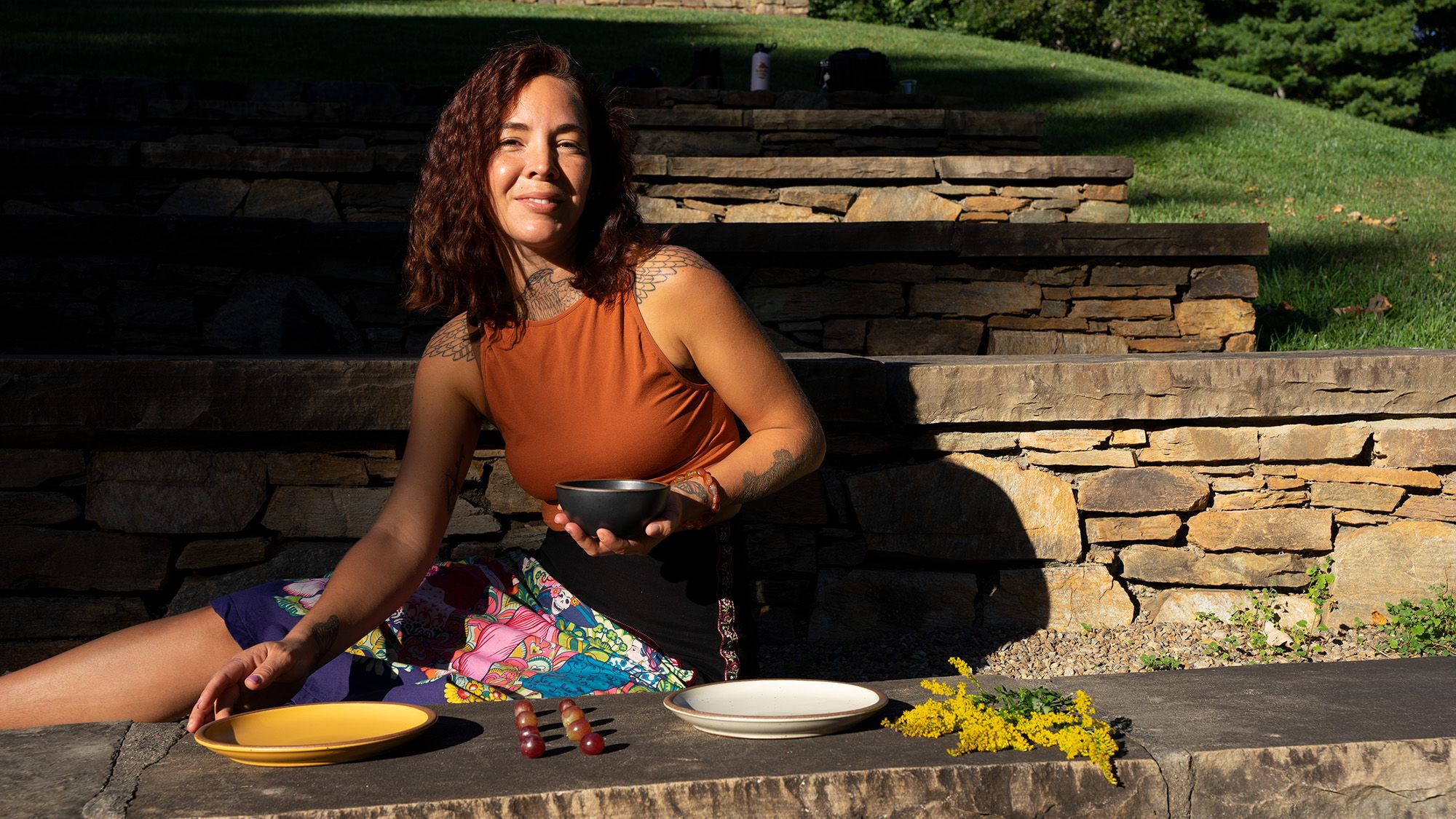 A person sits outside and is setting plates out on a long seat made of rocks
