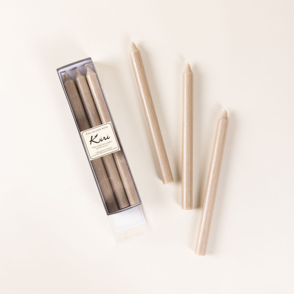A narrow box of beige taper candles, with 3 arranged outside of the box.