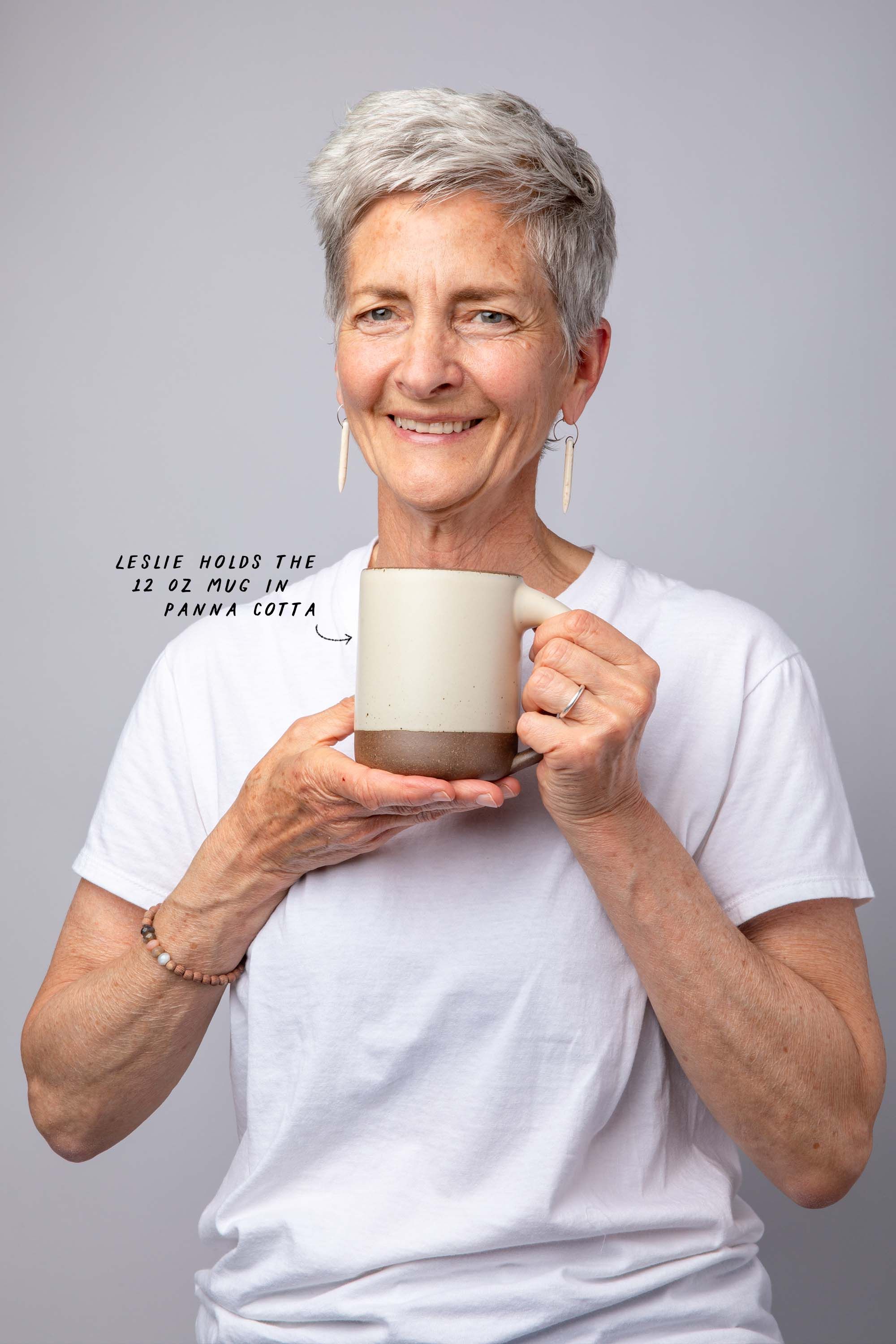 Woman with short gray hair holds The Mug and smiles