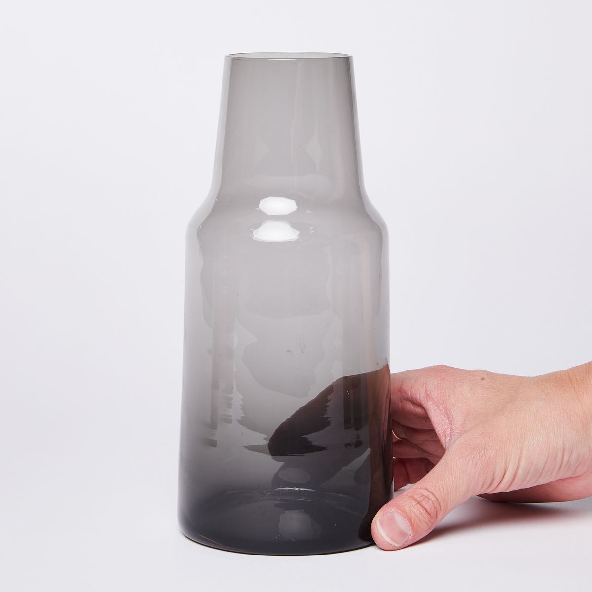 Hand holding glass carafe tapering at the top with a dark black bottom getting lighter grey towards the top