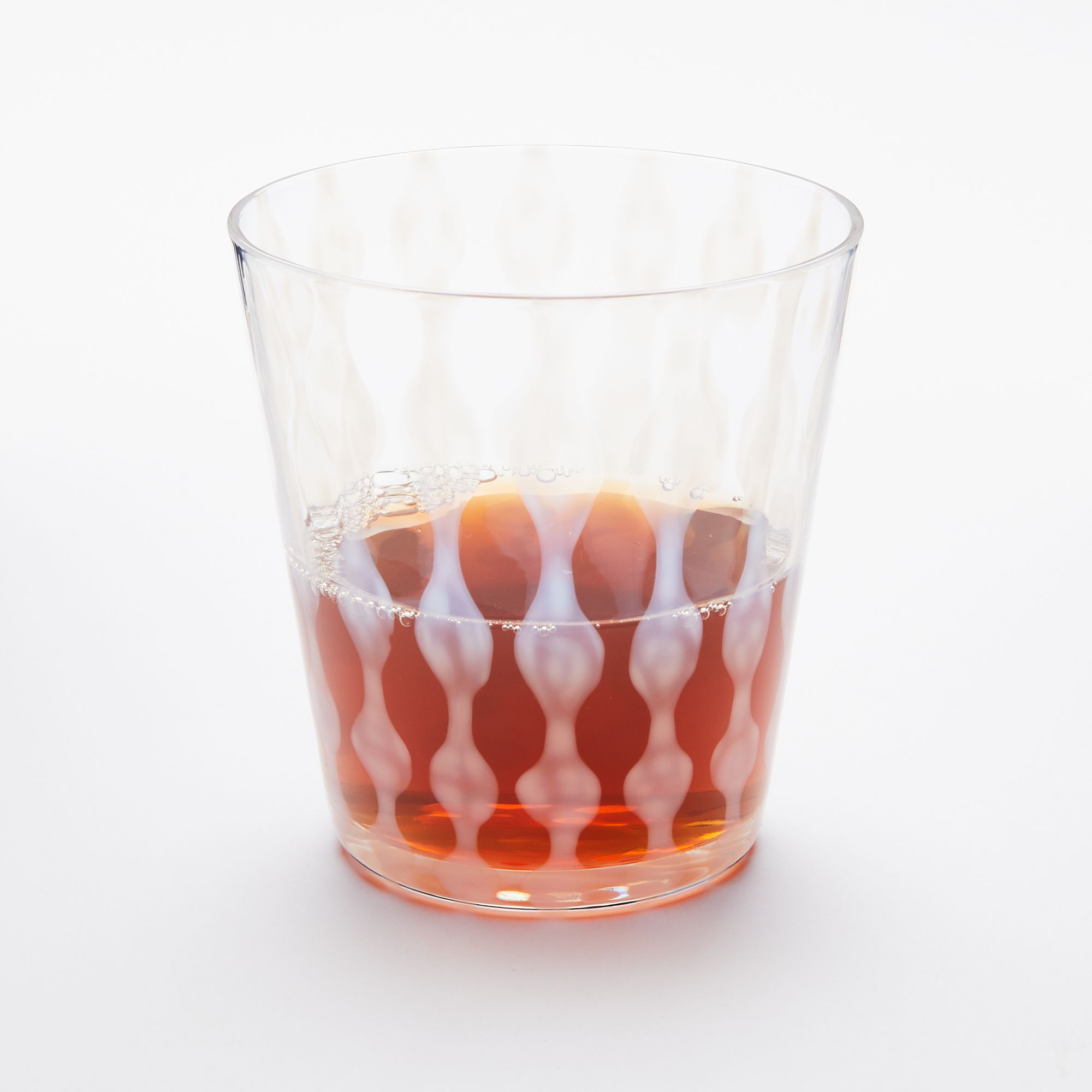 A short clear glass with a delicate vertical wave pattern, half filled with a drink