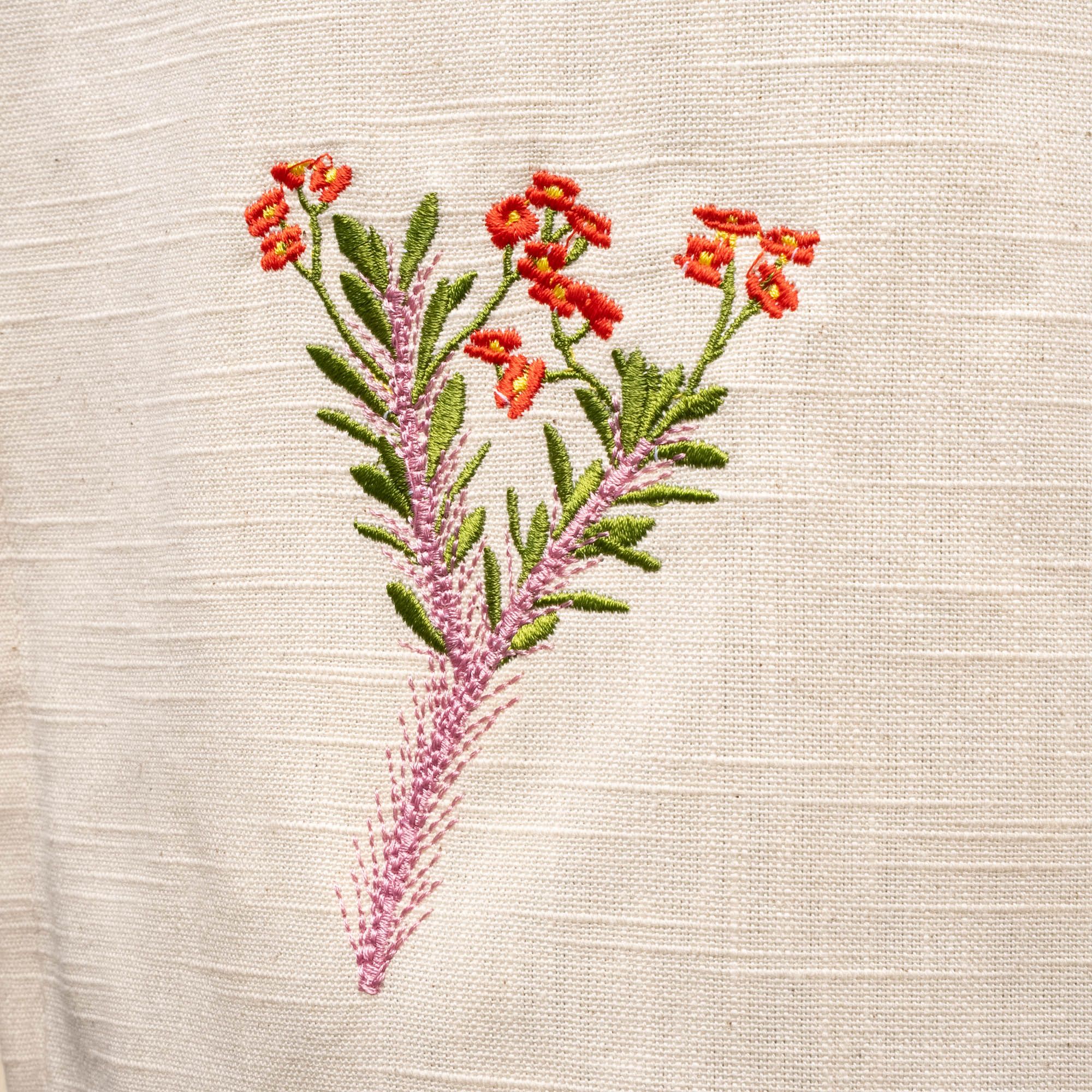A close up of a red, pink, and green embroidered flower on a canvas apron.