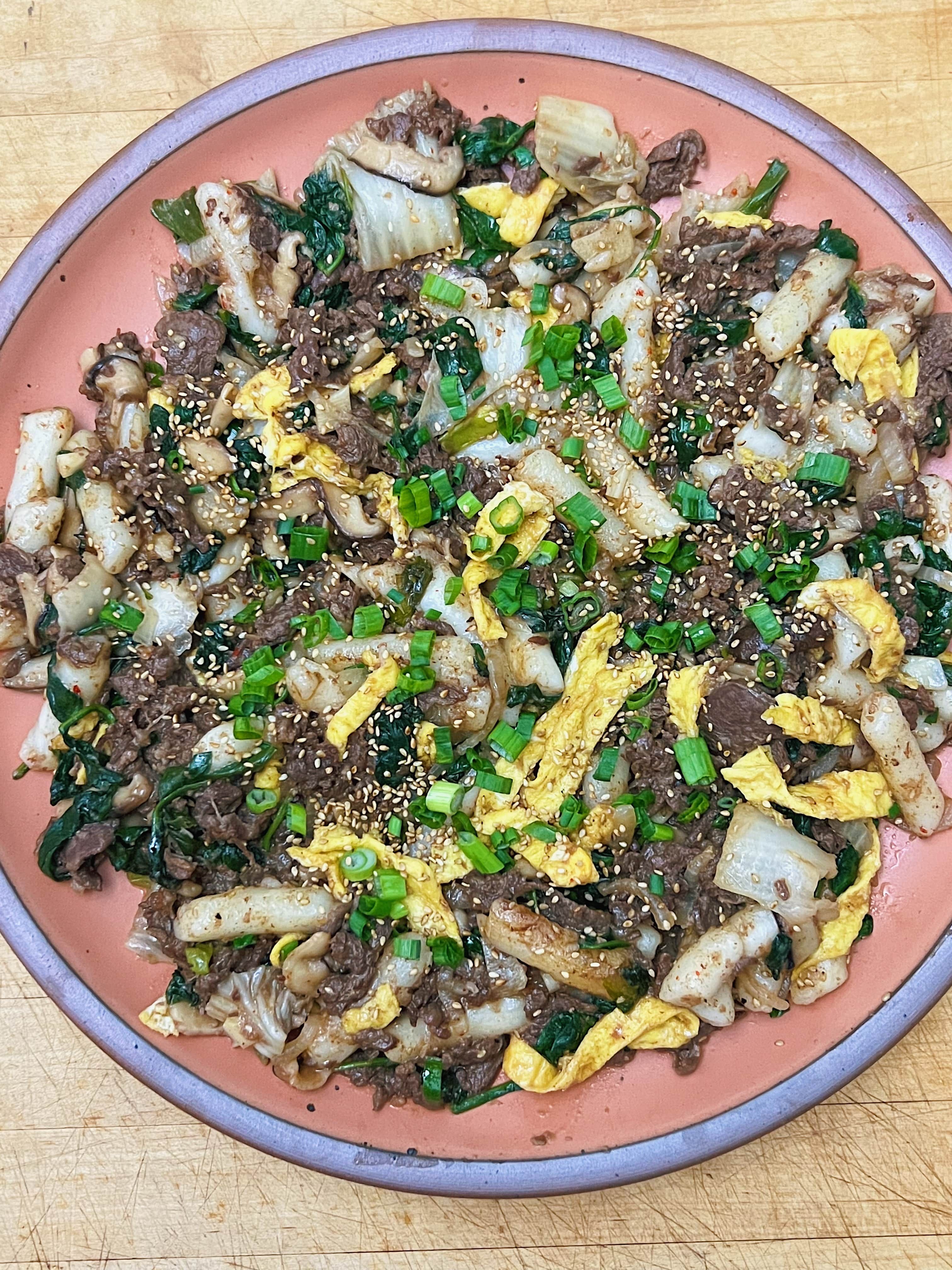 A ceramic plate in a peach color is plated with Brown Butter Bulgogi Tteokbokki