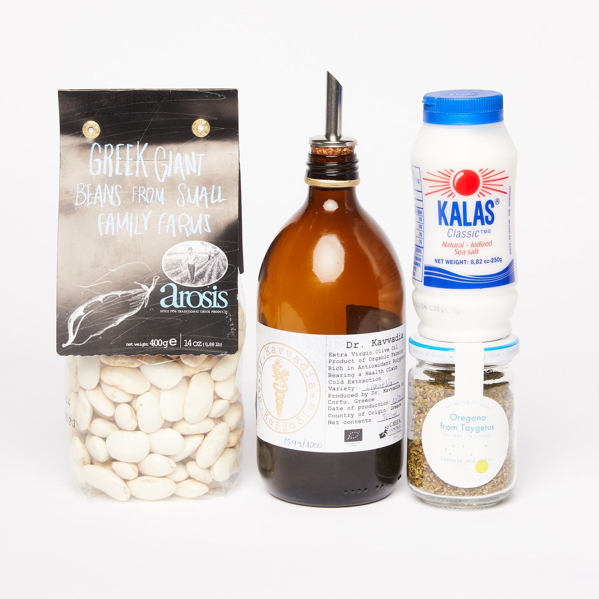 A clear bag of white gigante beans, a brown bottle of olive oil with pourer, a white bottle of salt on top of a clear jar of oregano