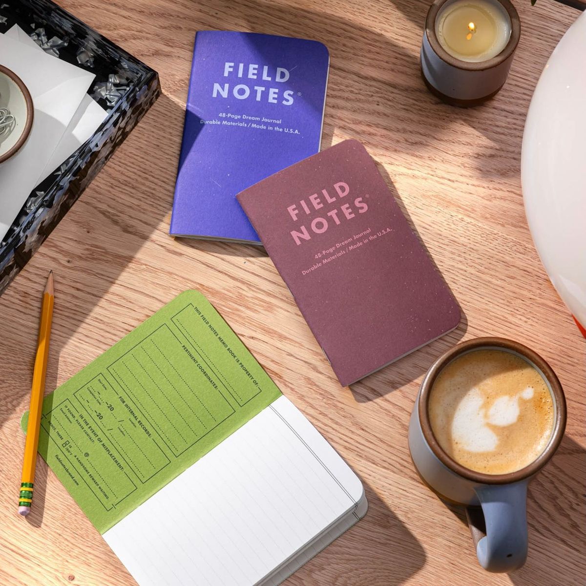 A mug filled with coffee 3 Pocket sized journals on a desk with 1 journal open showing lined pages