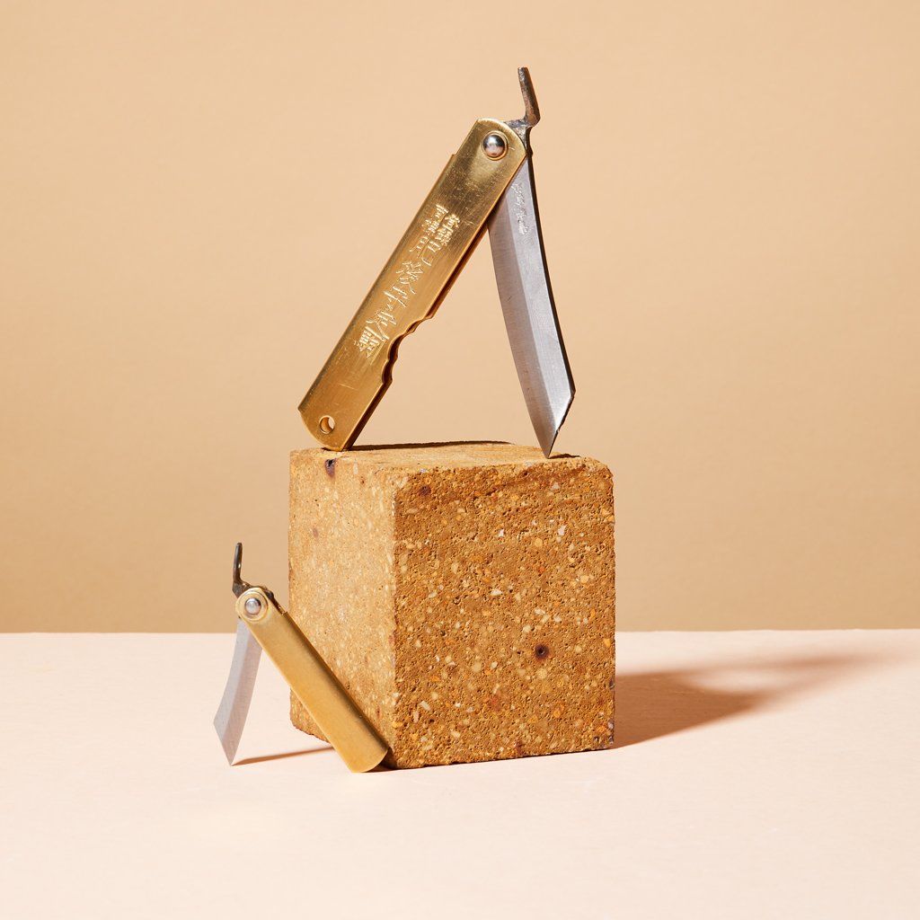 A large brass pocket knife atop a cork block with another pocket knife, smaller size, to the left