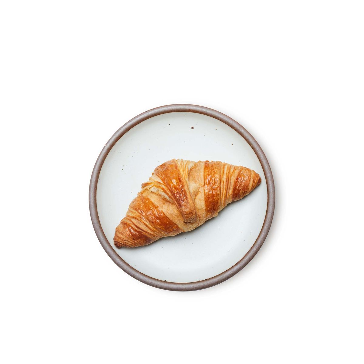 A croissant on a medium sized ceramic plate in a cool white color featuring iron speckles and an unglazed rim.