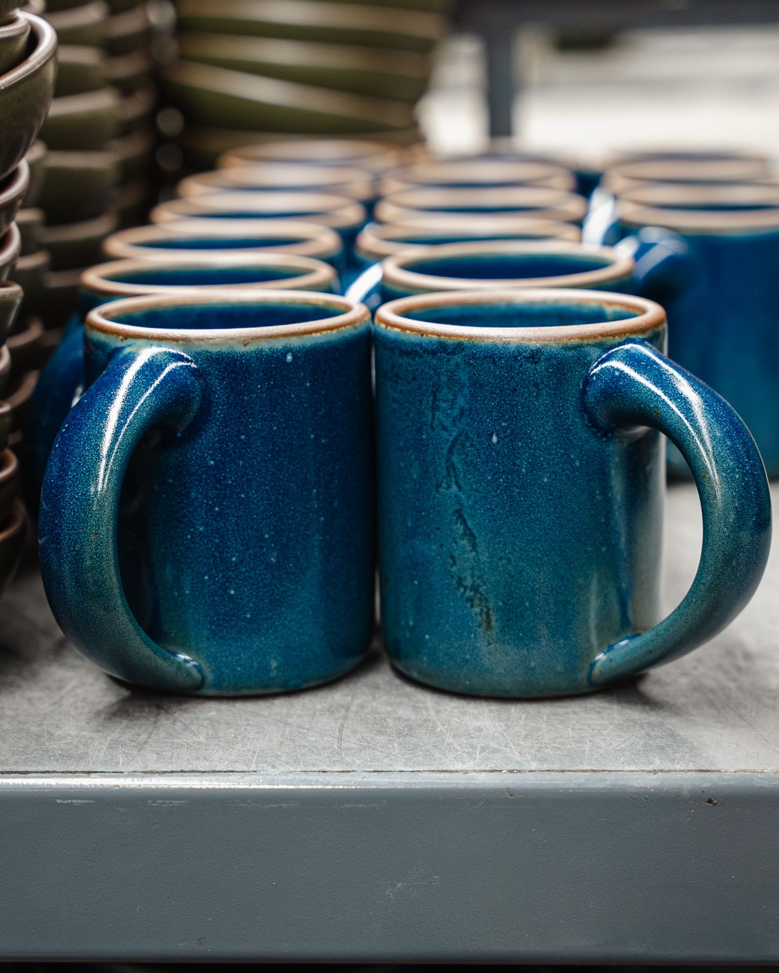 3 rows of ceramic mugs in a dappled glossy blue on a metal shelf