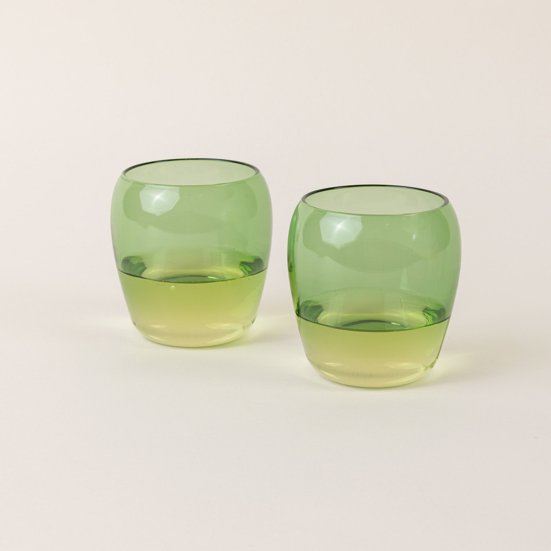 Two short light green glass tumblers with a slight curve inward on the top.