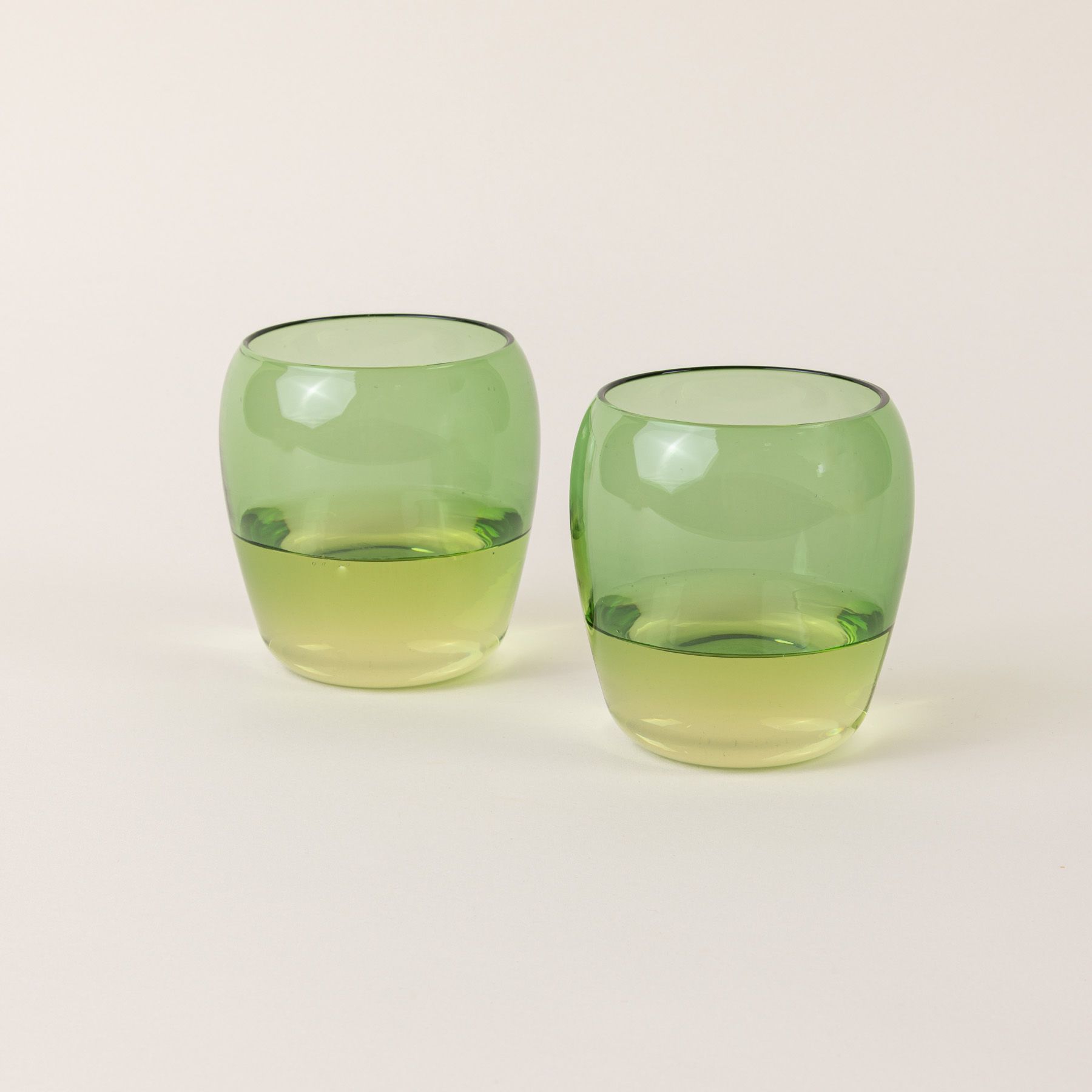 Two short light green glass tumblers with a slight curve inward on the top.