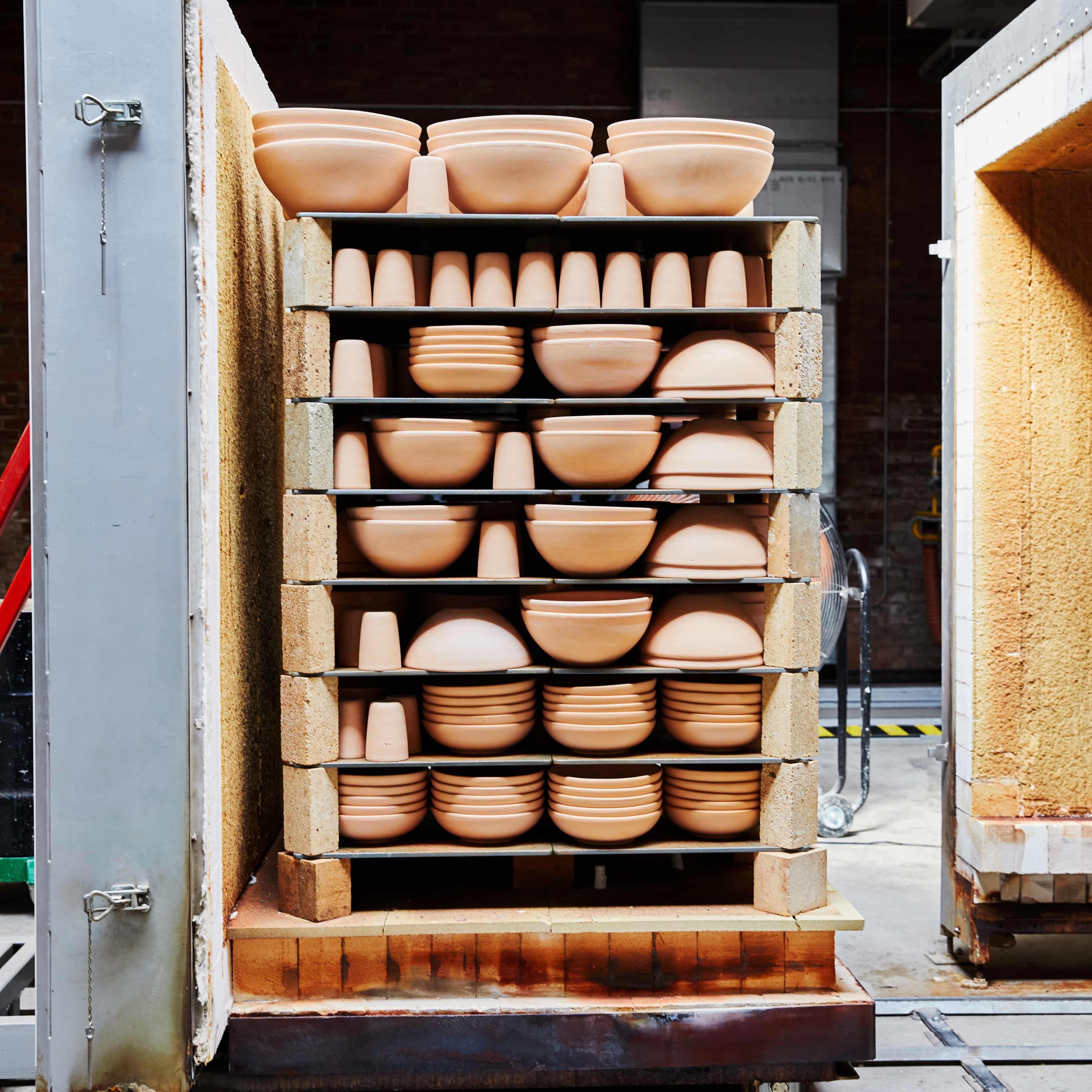 In a factory setting, there is a kiln cart filled with ceramic bisqueware large bowls and utensil holders.