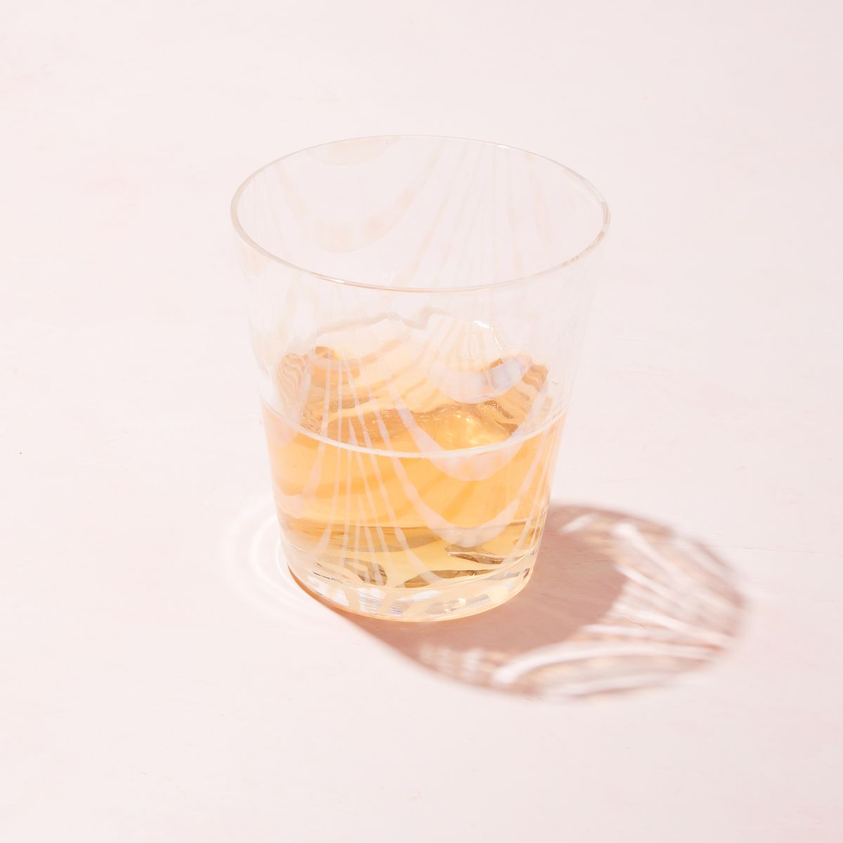 A short clear glass with a delicate ripple pattern, half filled with a drink and casting a shadow