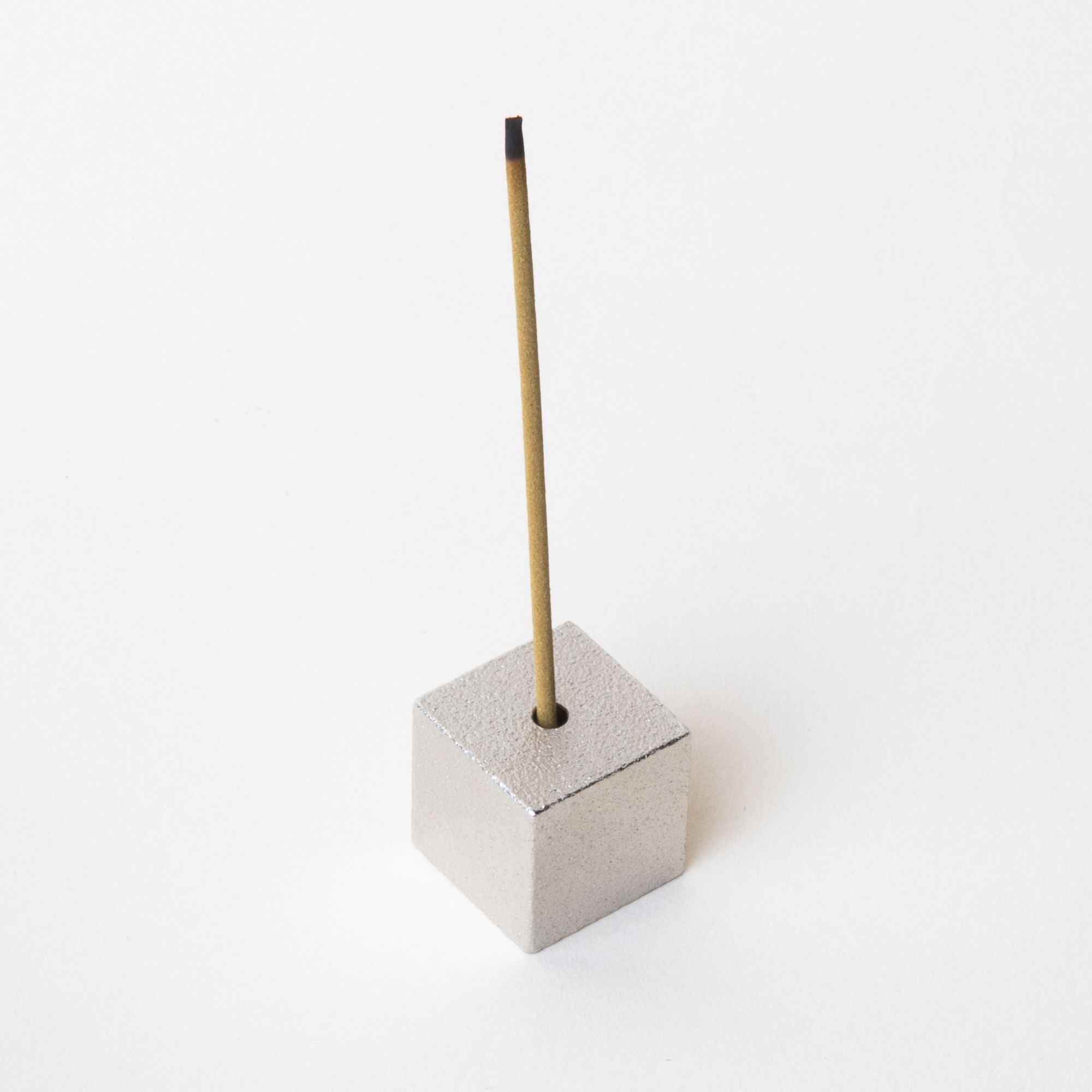 Minimal cube made of pewter with incense sitting on top