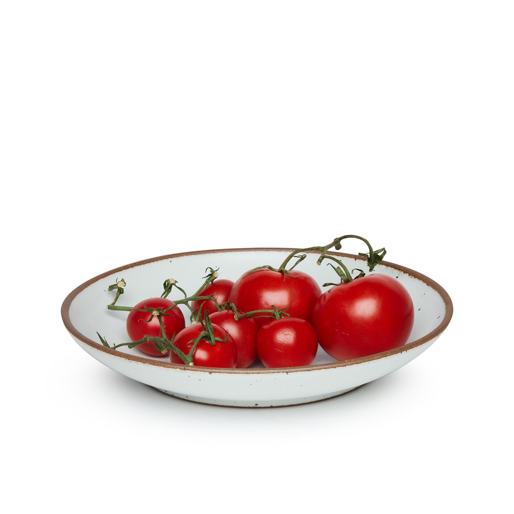 Tomatoes on a large ceramic plate with a curved bowl edge in a cool white color featuring iron speckles and an unglazed rim.