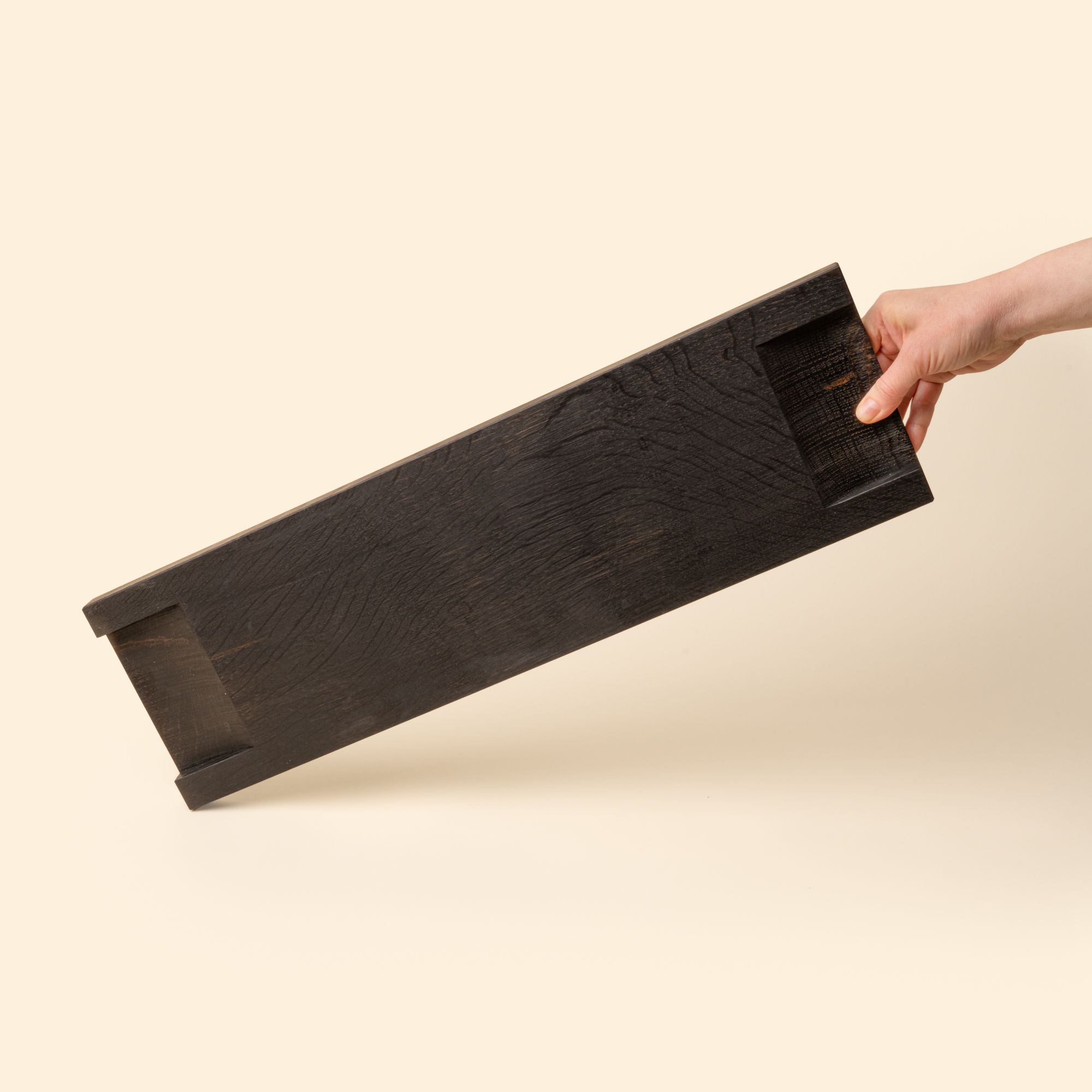 Hand holds out the back of a beveled narrow rectangle of ebonized oak wood
