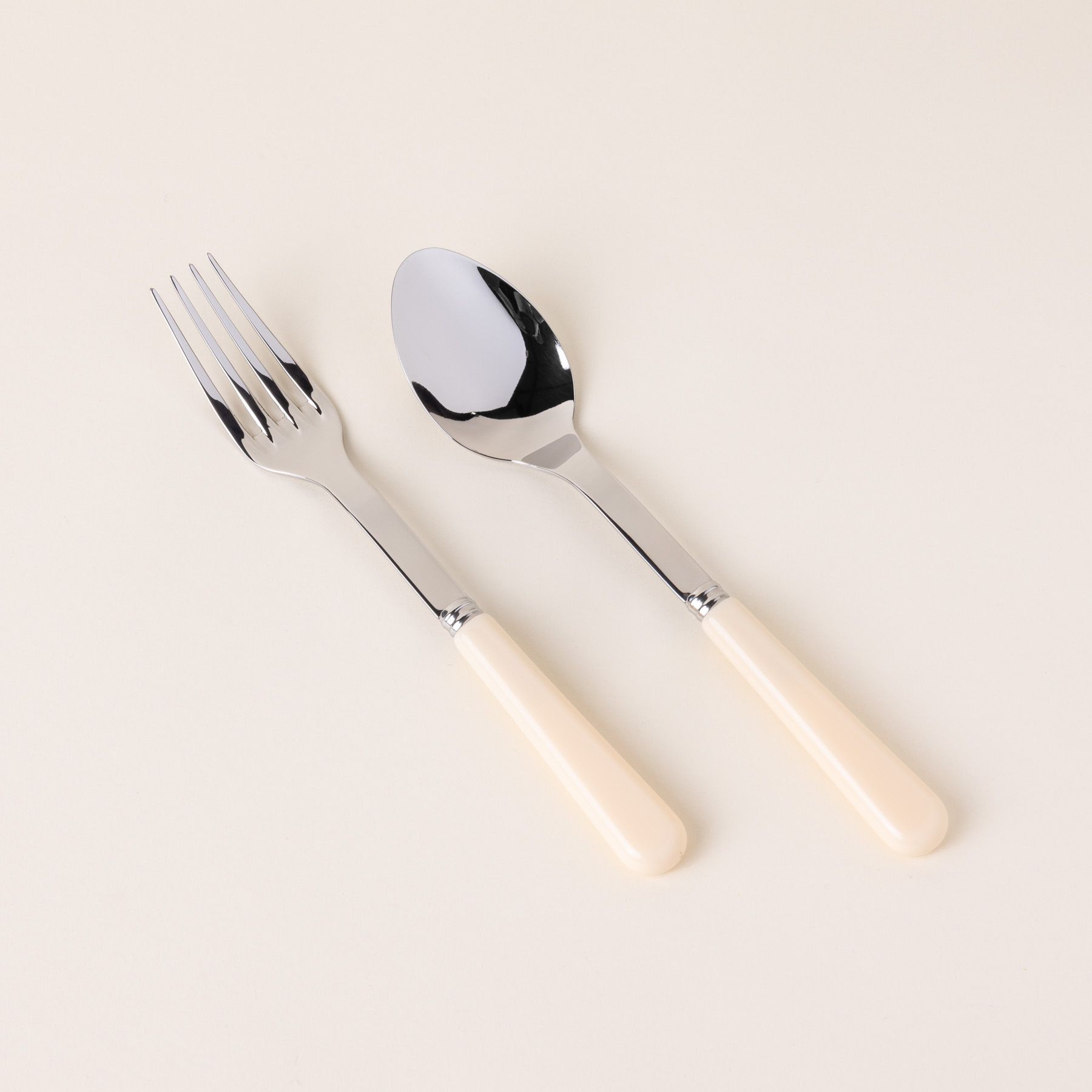 A serving size spoon and fork in a shiny steel with a matte cream handle