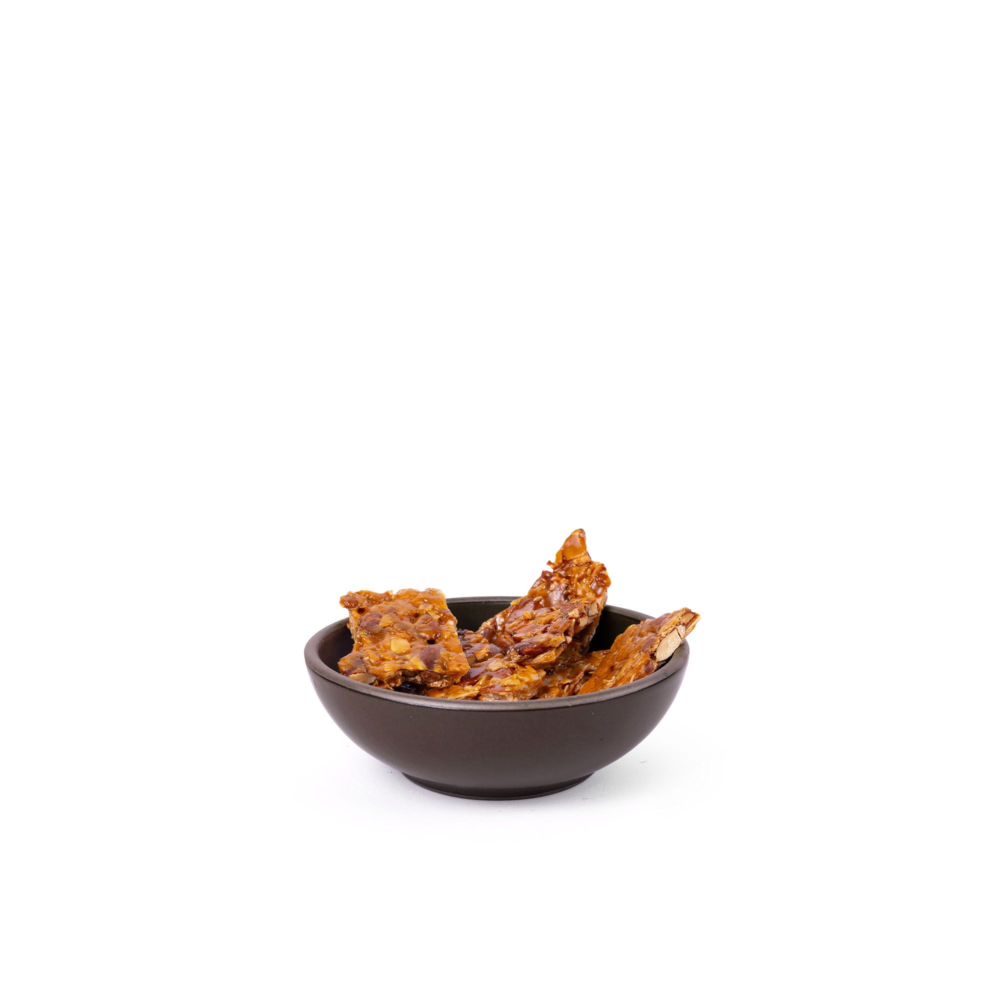 Peanut brittle in a small shallow ceramic bowl in a dark cool brown color featuring iron speckles and an unglazed rim